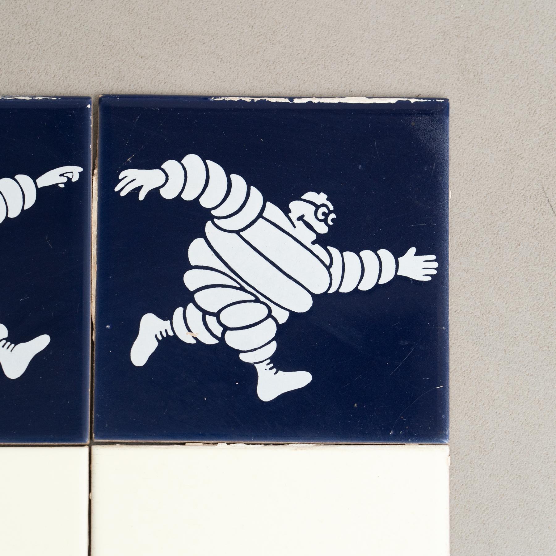 Embark on a journey of vintage charm with this exceptional set of tiles, featuring the iconic Michelin Man in a vibrant blue centerpiece, surrounded by original yellow tiles. Crafted by an unknown manufacturer in Spain circa 1960, this set is a