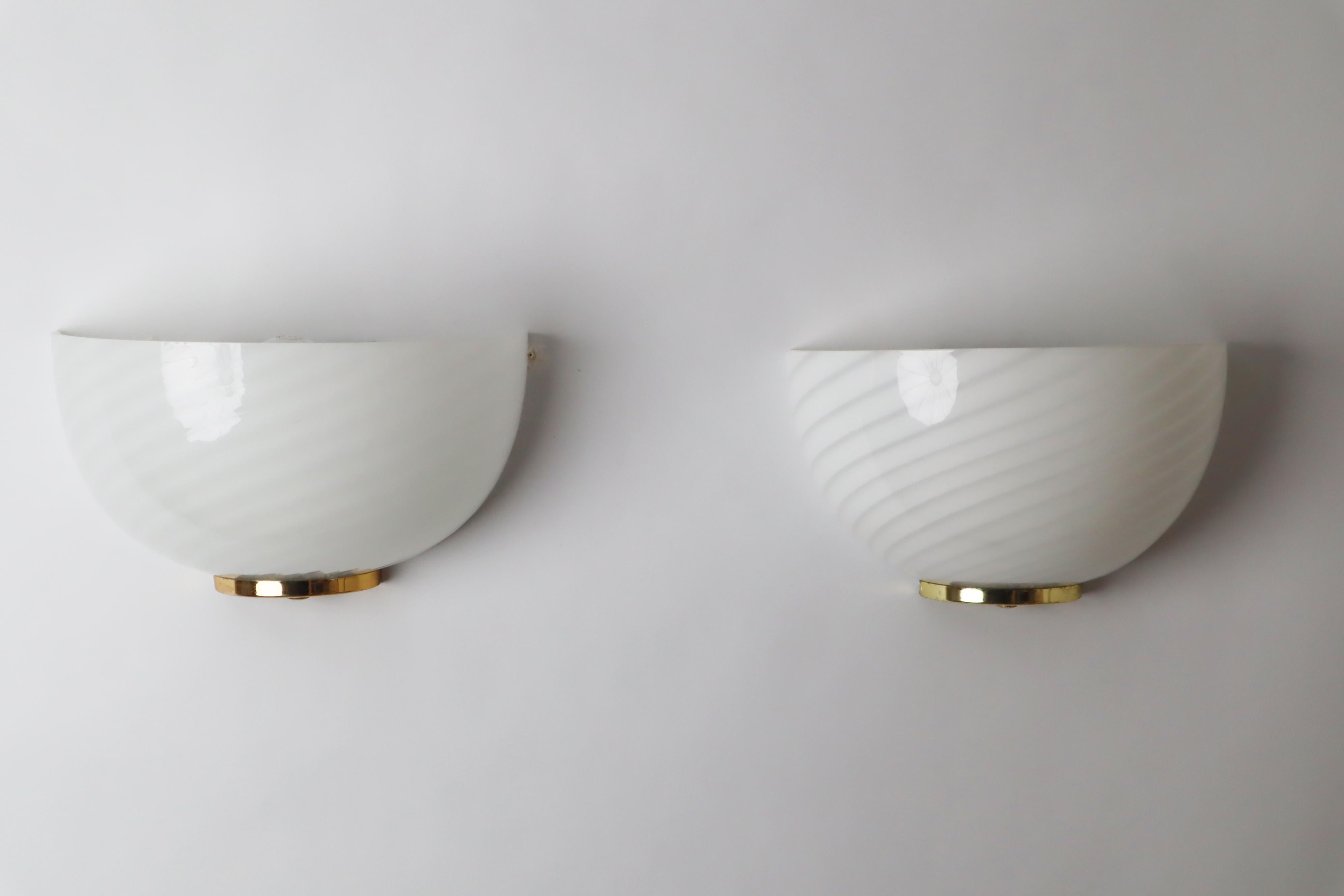 Schönes Set von weißen Murano-Wandleuchten im Vintage-Stil. Dieses Set stammt aus den 80er bis 90er Jahren. Das Glas ist kunstvoll zu einem weißen Wirbel geformt, die Befestigung besteht aus weiß lackiertem Metall, der untere Teil aus goldfarbenem