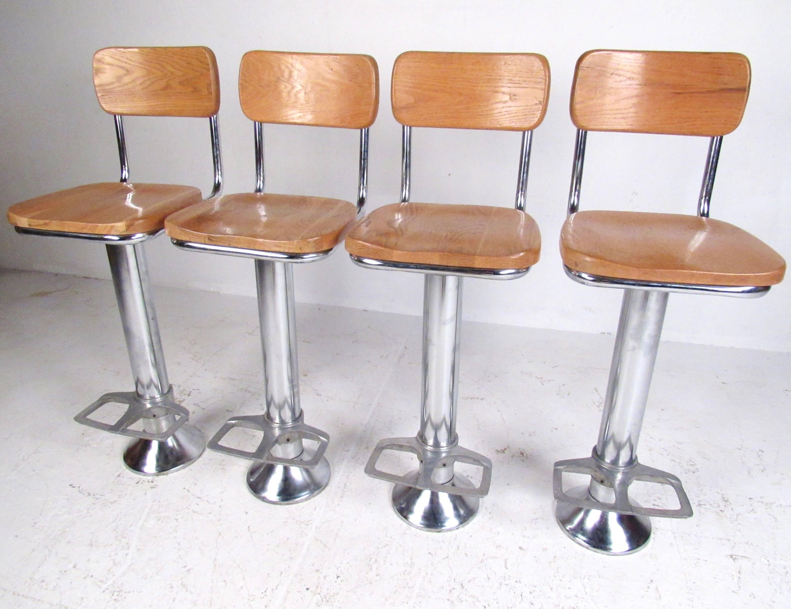 This set of four vintage barstools feature swivel pedestal design with sculpted oak seats and backs. Substantial construction, built-in footrest, and quality Industrial modern style. Impressive set of stools ready to be bolted in for home or