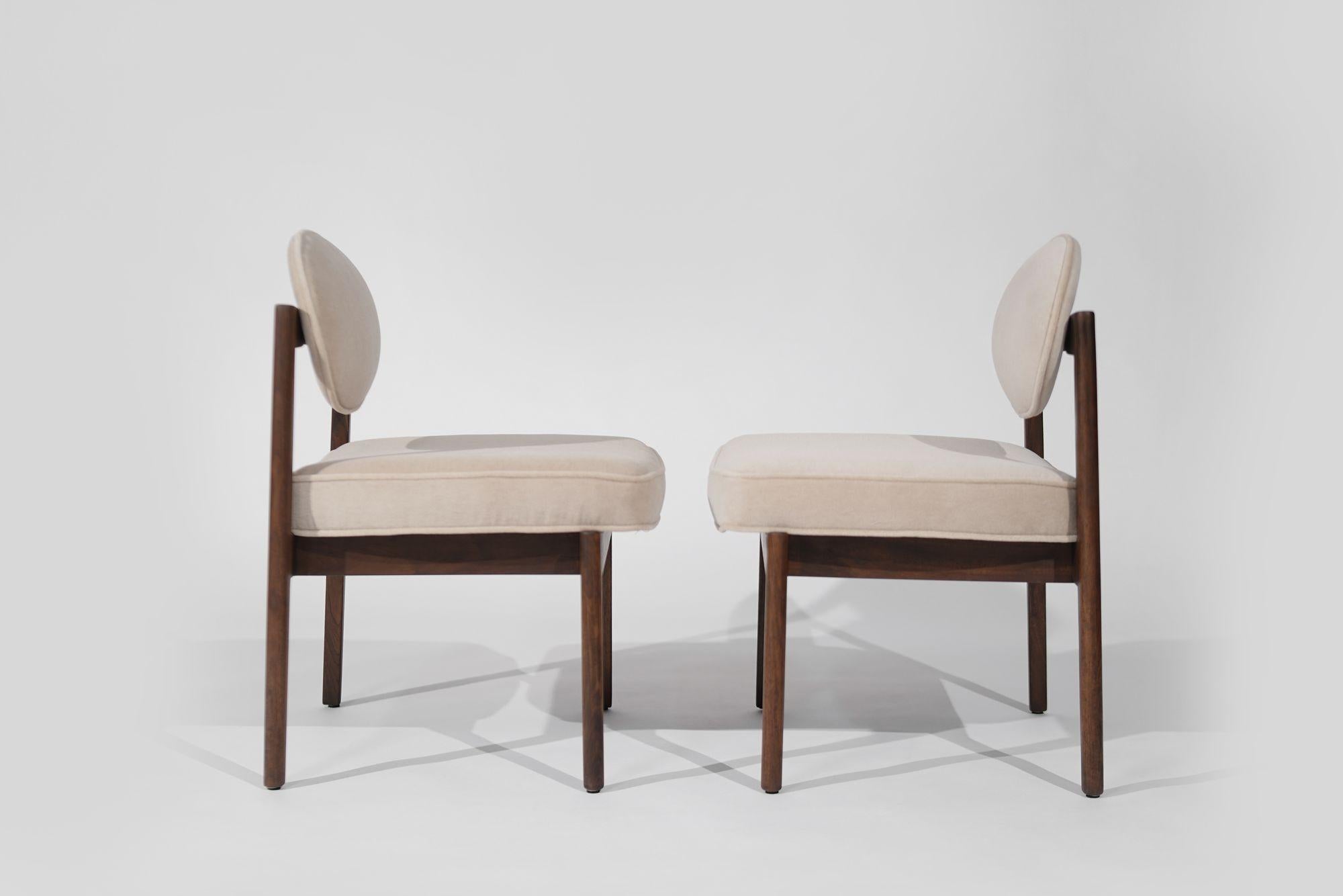 An exquisite pair of mid-century modern side hairs designed by Jens Risom, crafted circa 1960-1969. Meticulously restored, the walnut framework shines with renewed beauty, complemented by a luxurious reupholstery in natural mohair. A perfect blend