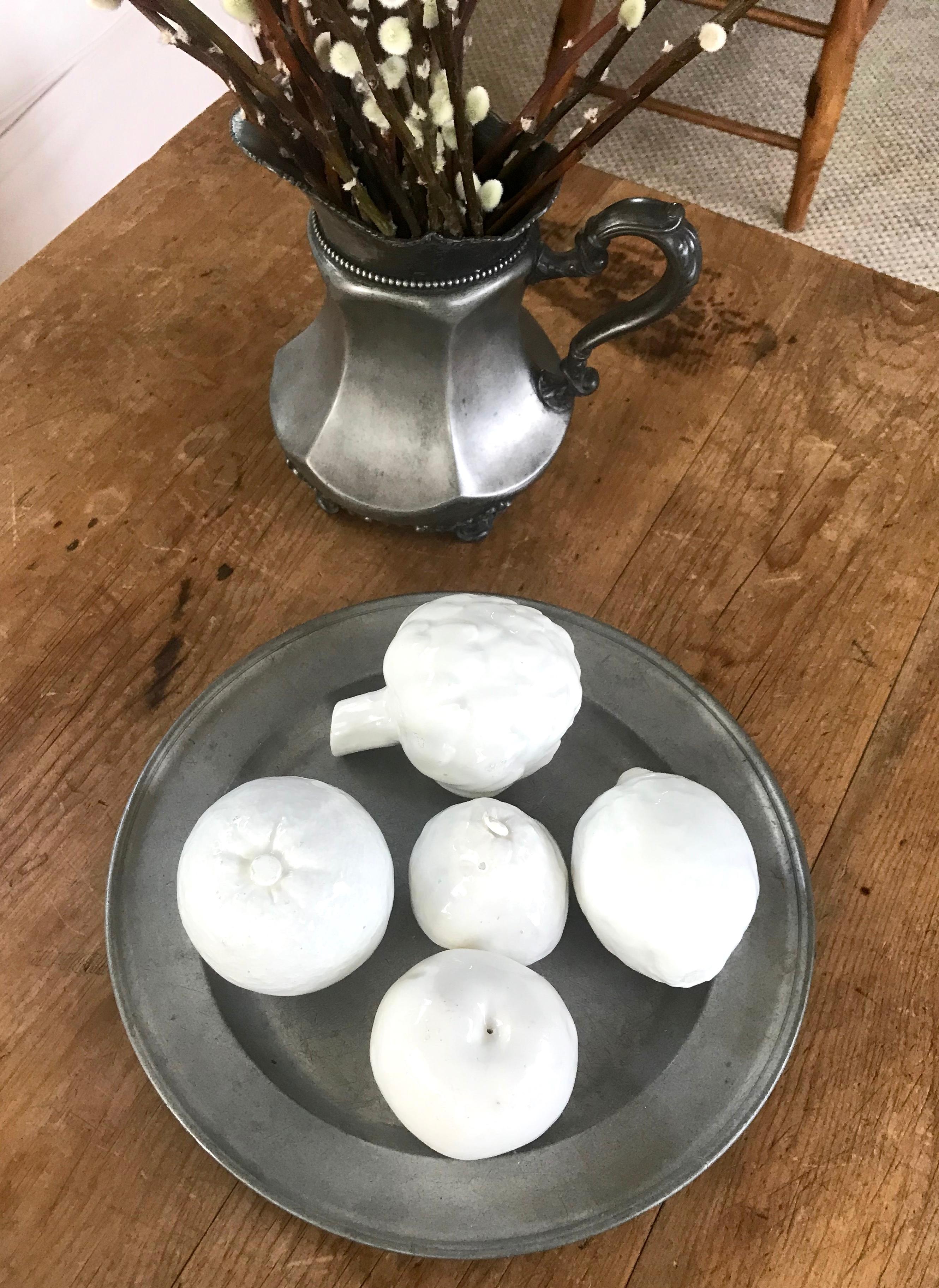 Set di frutta in ceramica spagnola smaltata di bianco. Cinque pezzi di frutta modellata a grandezza naturale con smalto bianco lucido: mela, carciofo, limone, arancia e pera. Piccole scalfitture sullo smalto alla base, ognuna con un segno
