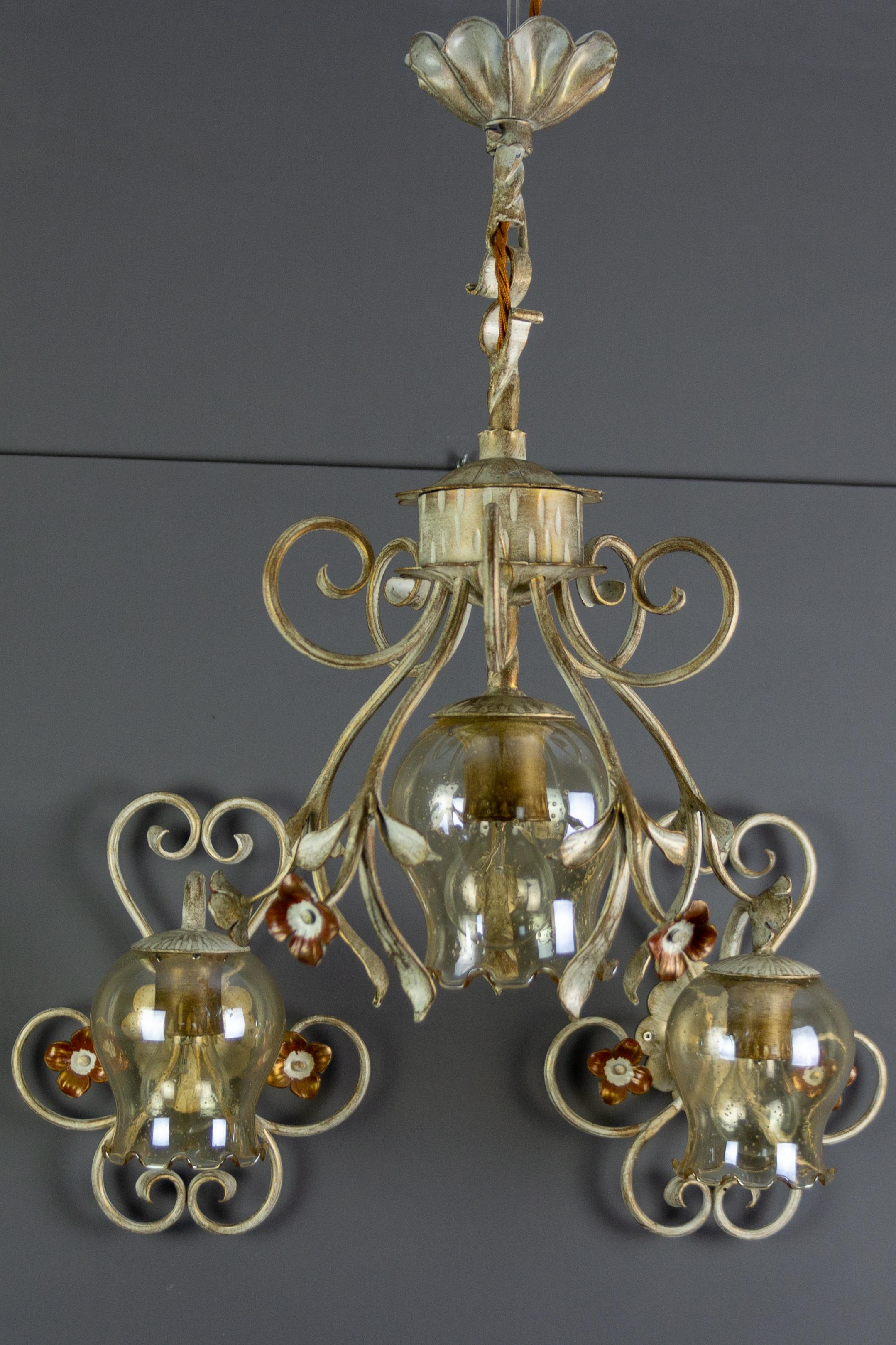 This adorable German blacksmith artwork set consists of one pendant light fixture and two wall sconces. Light fixtures are made of white and golden patinated wrought iron, each with a smoky glass lampshade and beautiful floral decors.
Each lamp has