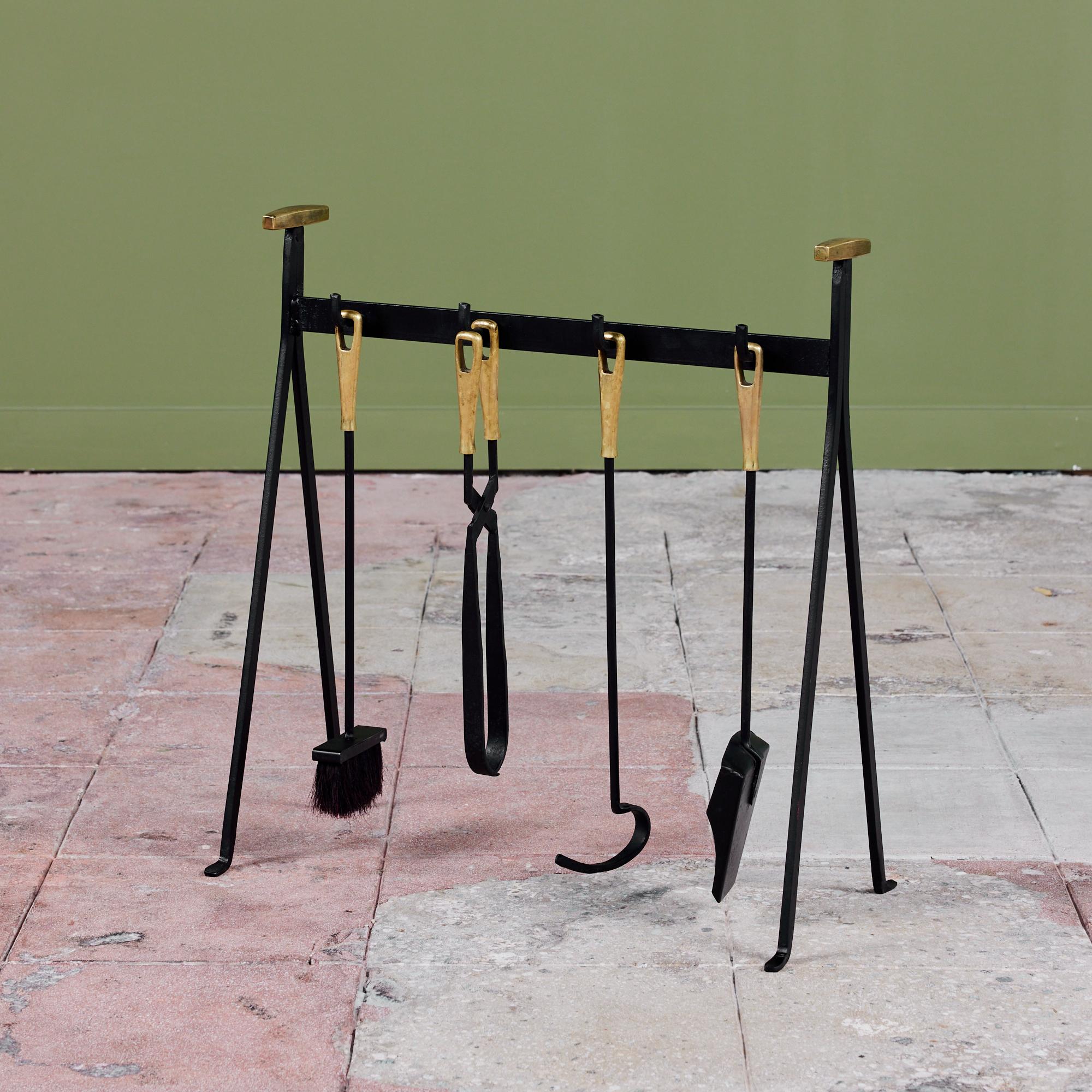 Four piece set of fireplace tools with stand from notable Danish retailer Illums Bolighus located in Copenhagen. The set features four tools each with a brass handle on a triangular stand. All elements are made of blackened iron. This modernist
