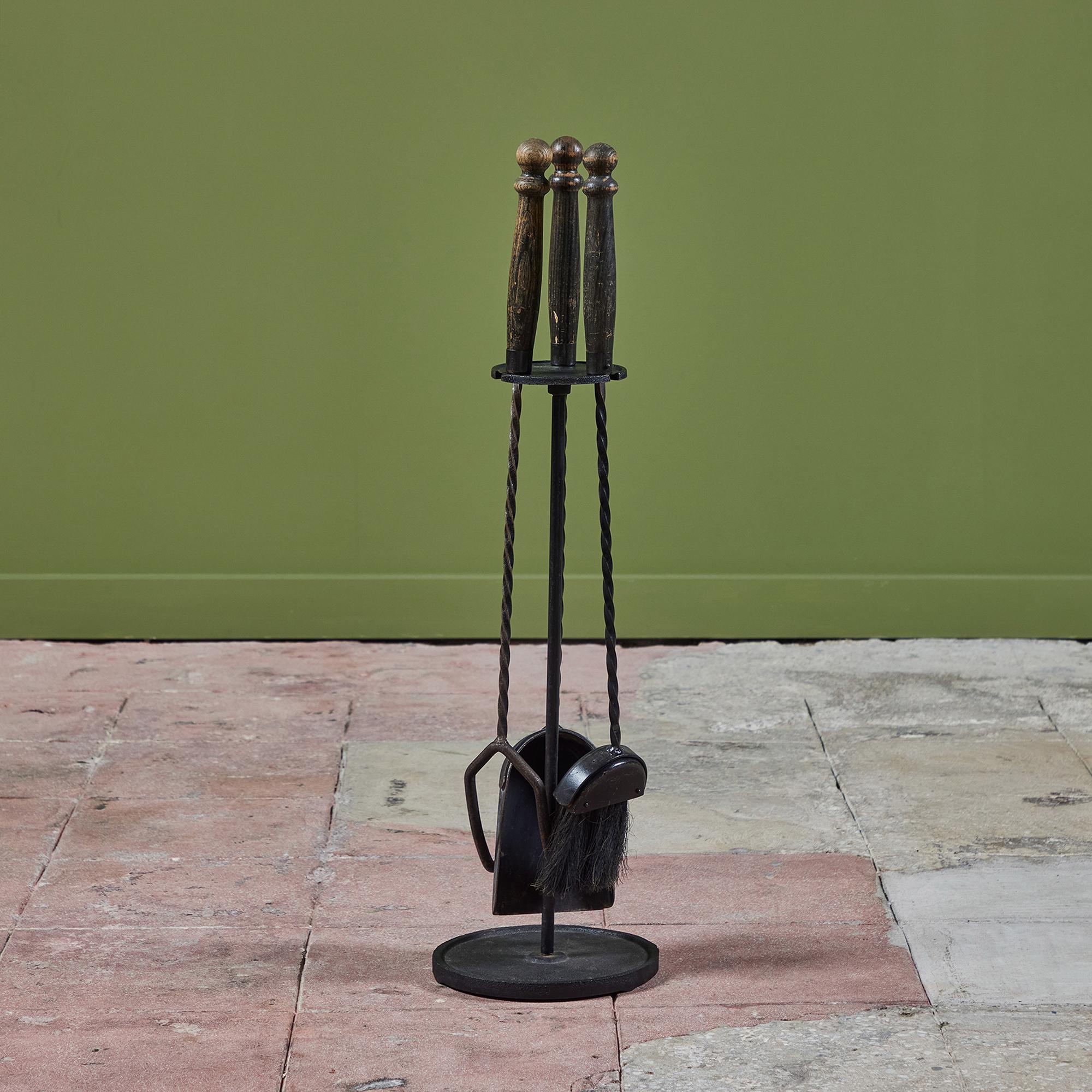 Three piece set of fireplace tools with stand. The set features three tools with carved wood handles and and twisted wrought iron stems on a rounded stand. All elements are made of blackened iron.

Dimensions
9