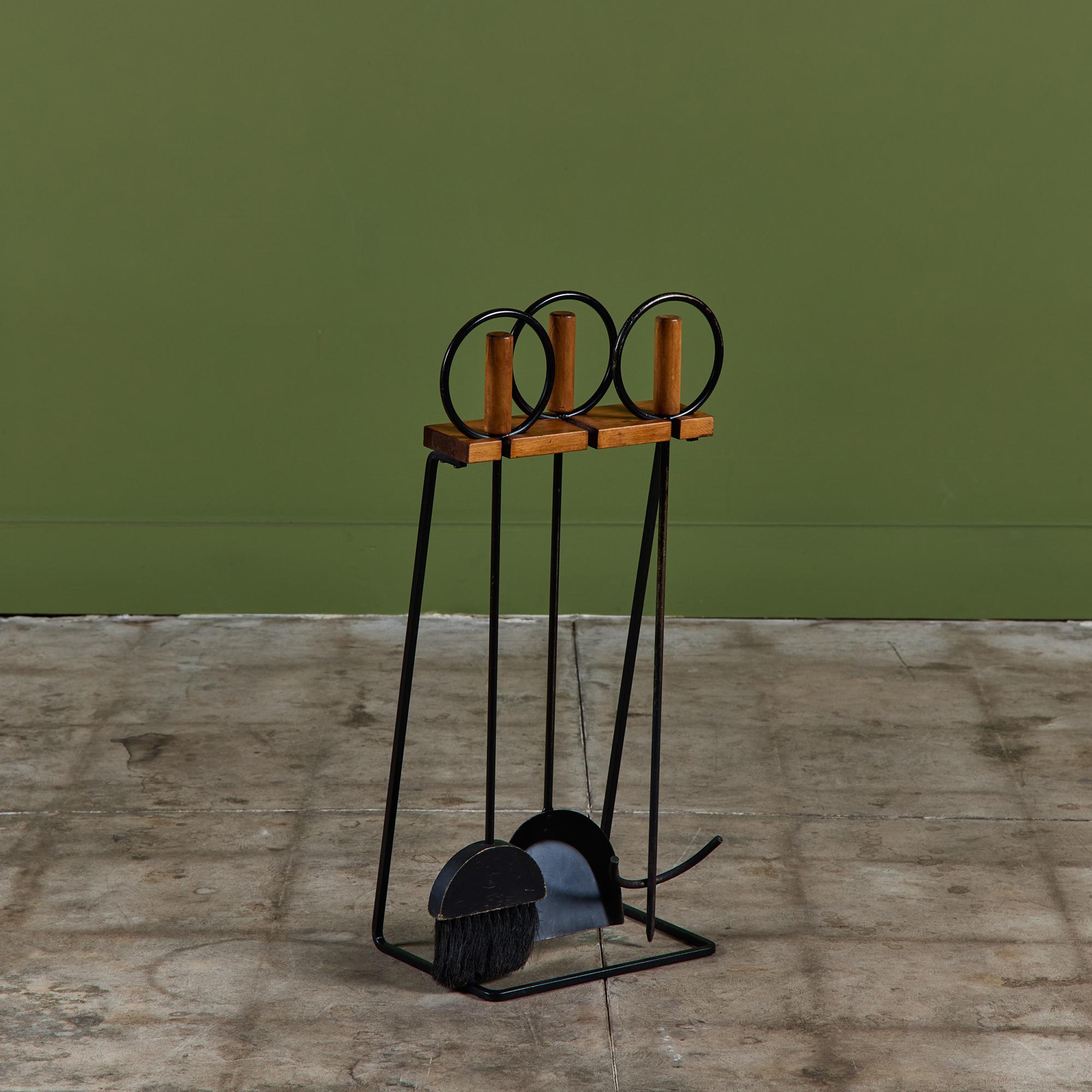 Three piece set of fireplace tools with stand. The set features three tools, a shovel, broom and poker. Each handle has a wood rod and circular wrought iron detail.  All elements rest on a cantilever wood and iron stand.

Dimensions
14.5” width x