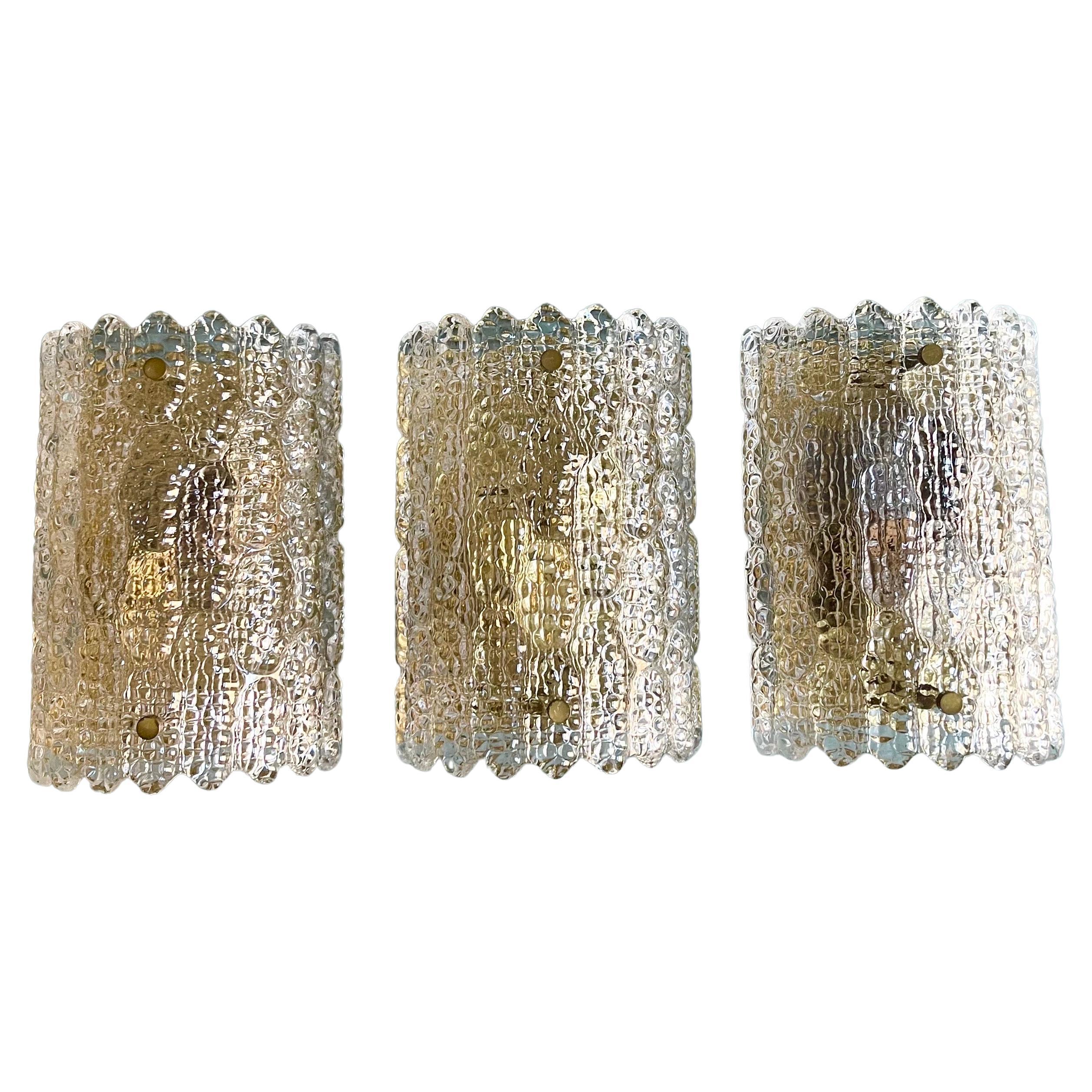 Set of three Mid-Century Modern wall sconces by swedish designer Carl Fagerlund for Orrefors.
It is composed of textured thick glass elements and polished brass hardware.
Socket: each 2 x E 14 for standard screw bulbs.