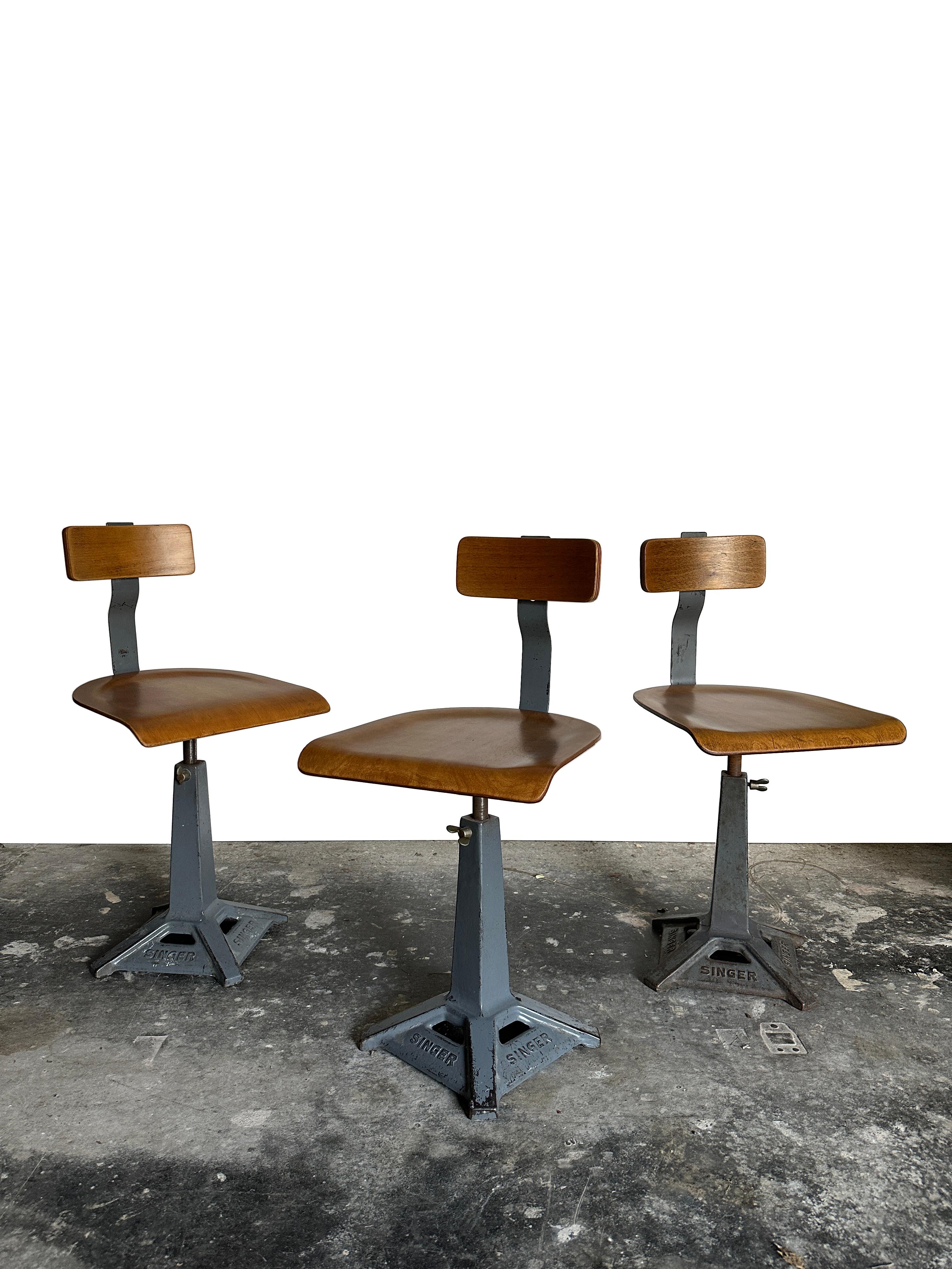 - A beautiful set of original Singer sewing chairs, England circa 1940.
- The chairs feature a branded heavy die-cast iron base in their original grey painted finish, and that hold a swivel mechanism to adjust the seating height.  Steam bent ply