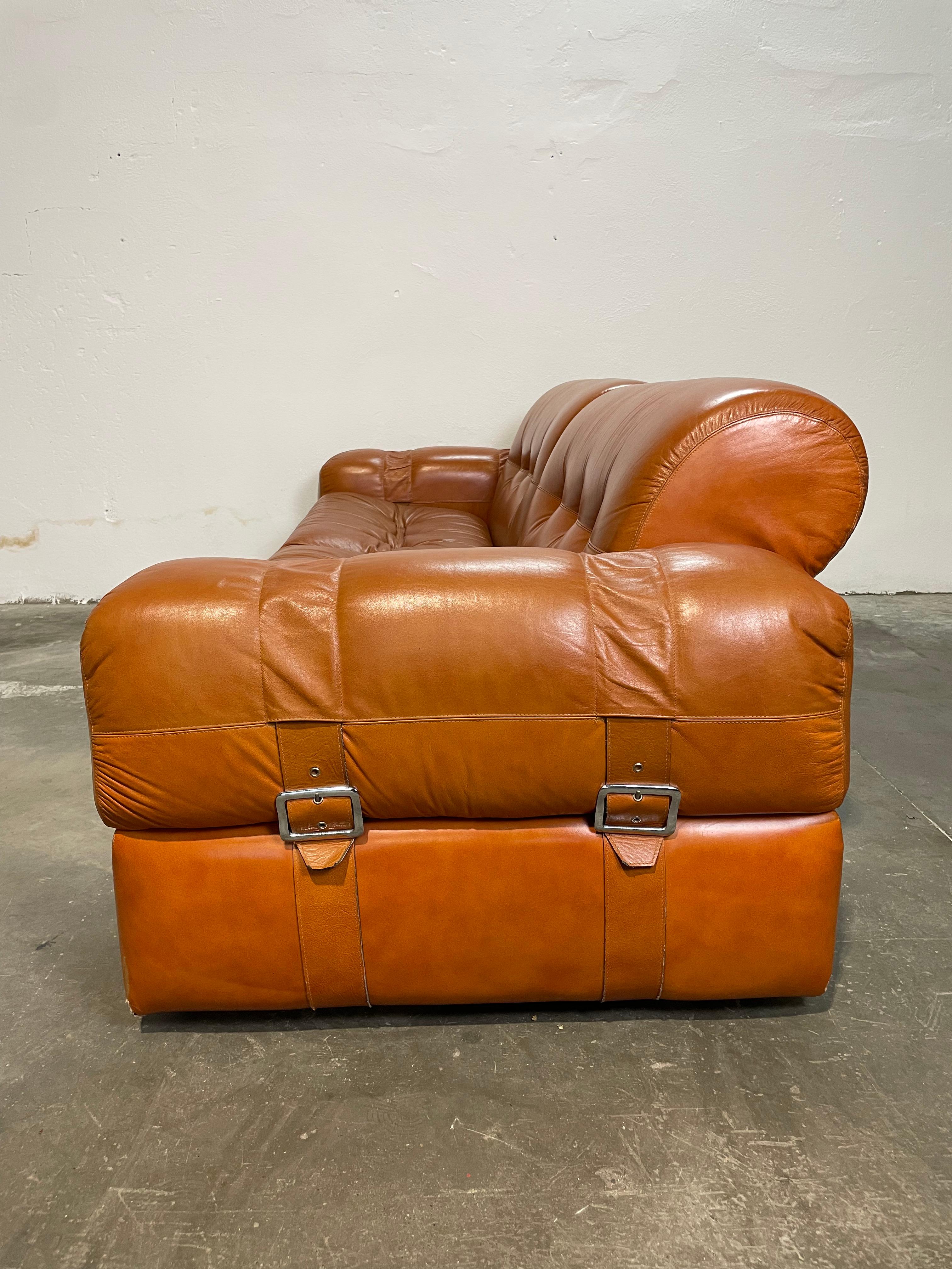 Splendido set di divano e due poltrone in pelle, colore arancio vibrante, firmato Adriano Piazzesi, icona del design anni '70. Mai usato, in condizioni impeccabili, questo ensemble rappresenta un autentico capolavoro vintage, perfetto per chi cerca