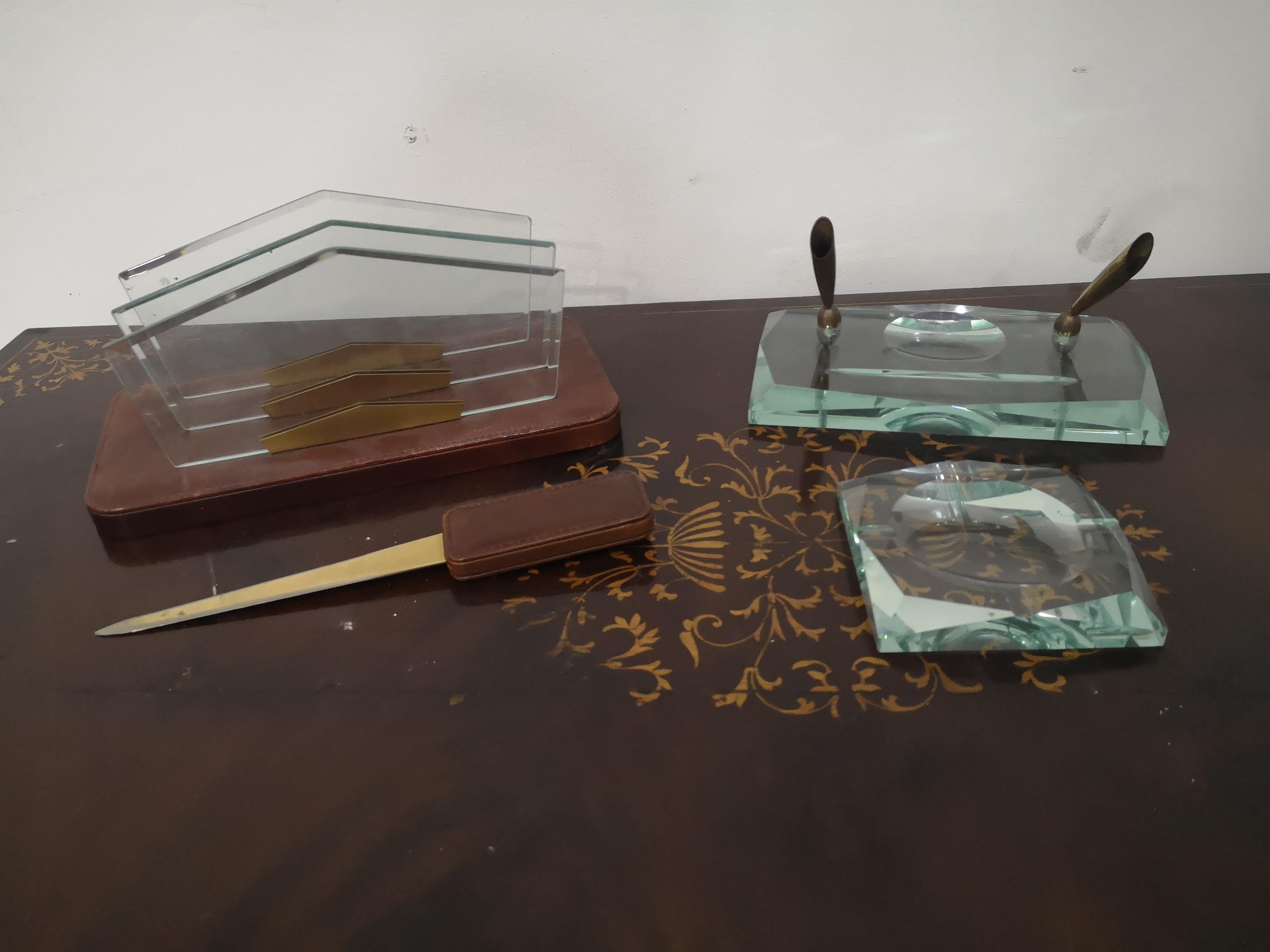 Schreibtischset aus den 70er Jahren, Fontana Arte zugeschrieben
bestehend aus:
Stifthalter aus Glas und Messing, 22 x 13 cm
Korrespondenzkasten aus Leder und Glas 28 x 14 cm
Glas-Aschenbecher 11,5 x 11,5 cm
Brieföffner aus Leder und Messing 26 cm -