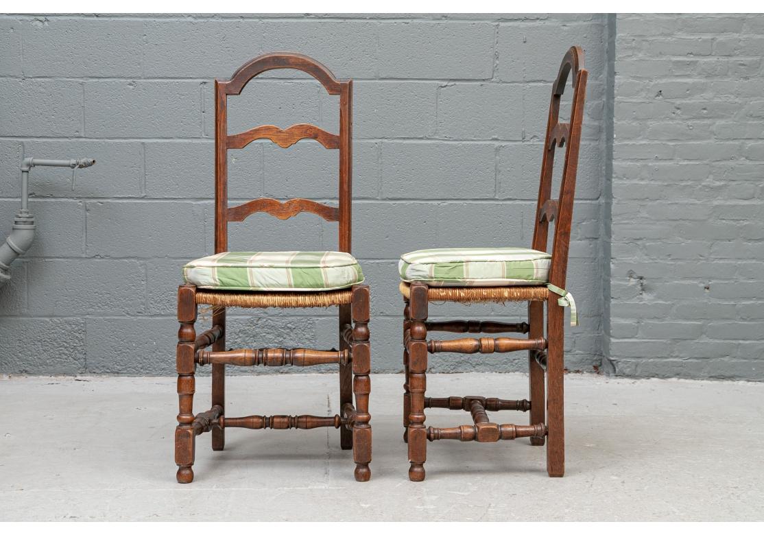 With arch shaped crest rails and shaped ladder backs. The rush seats raised on heavy turned legs with turned front and back stretchers and double side stretchers. Along with green and ecru plaid seat tie on cushions. 
H. 41 1/2