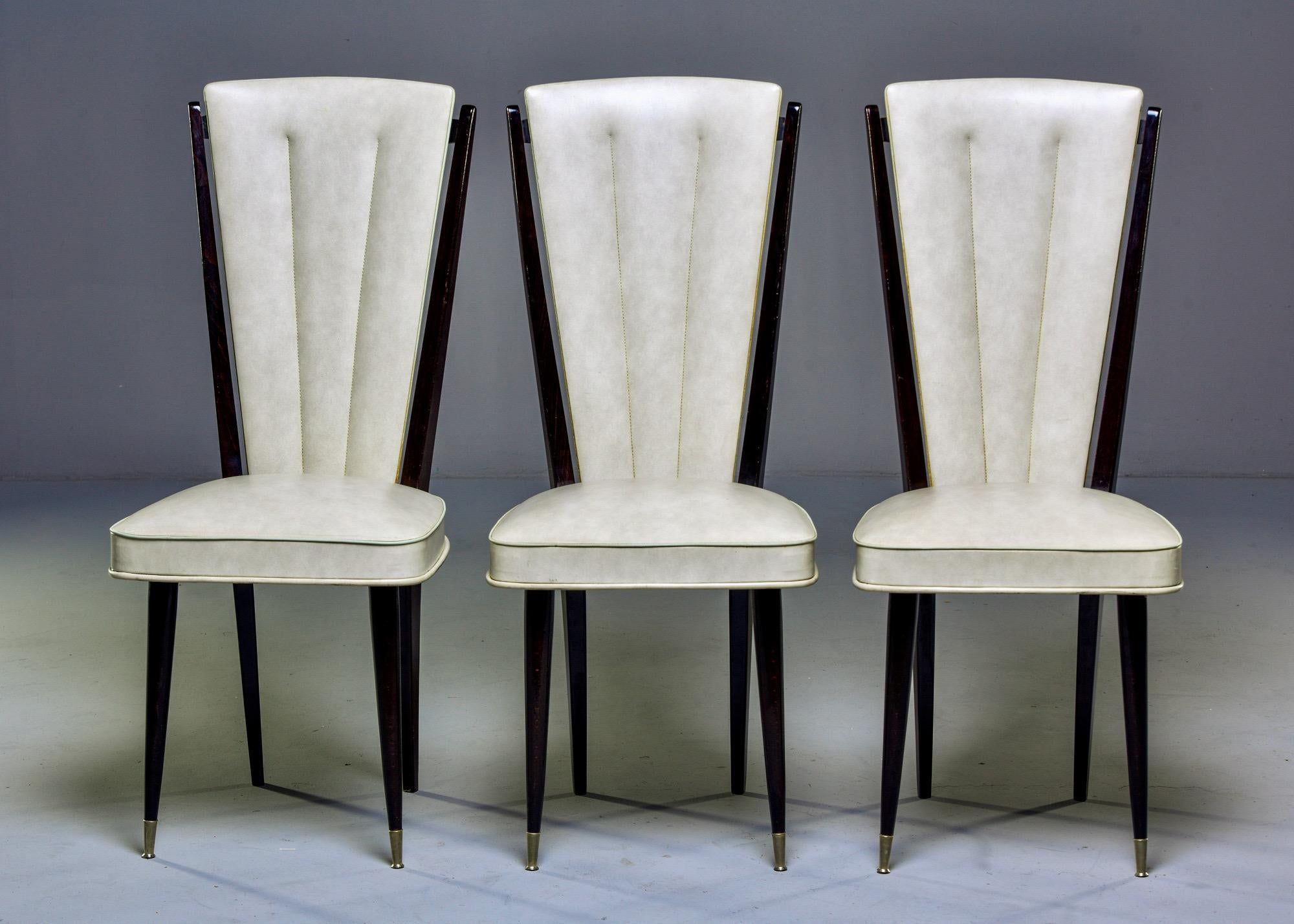 Set of French dining chairs with slender, dark-stained Macassar frames, circa 1950s. Tapered legs feature brass-capped front feet. Original white vinyl upholstery can be used as is, but these would be stunning in a new fabric of your choice. Unknown