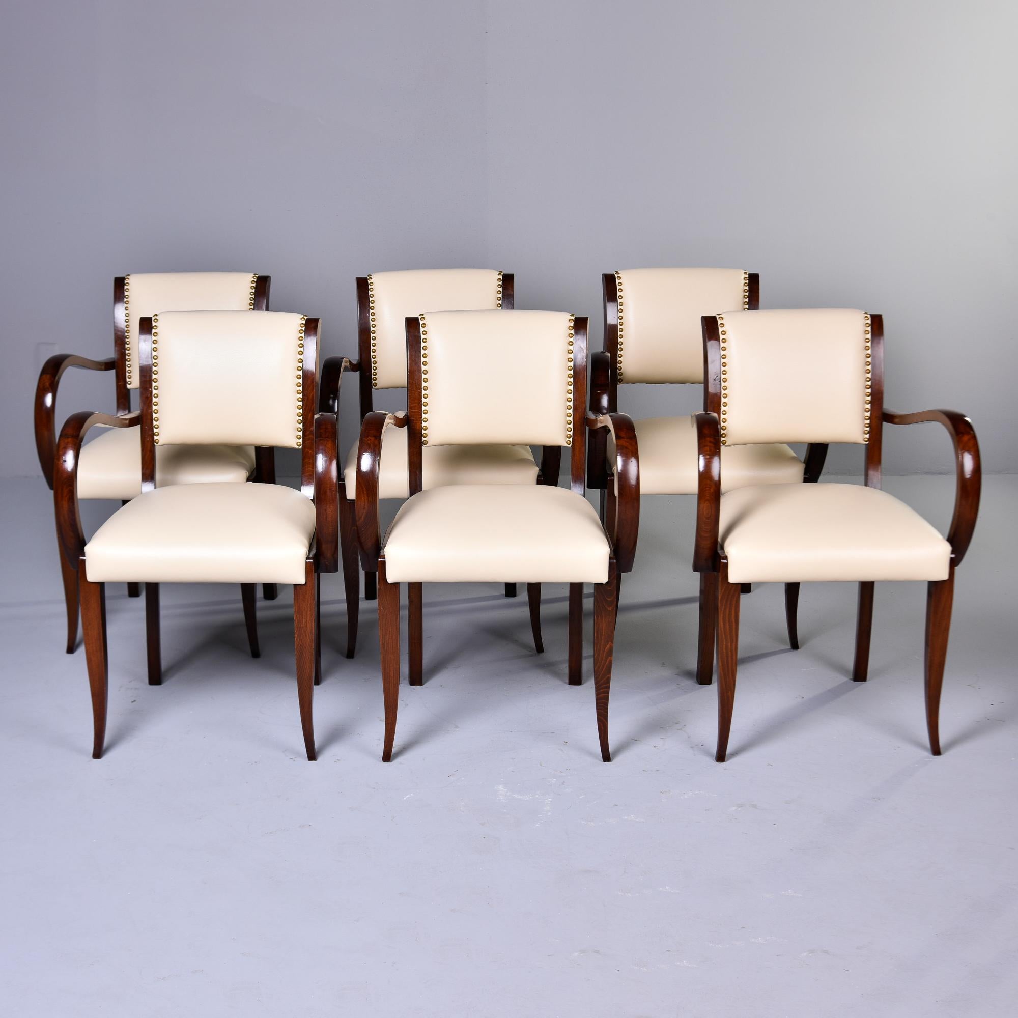 Found in France, this set of six chairs dates from the 1940s. Chairs have dark-stained walnut frames with tapered legs and dramatically curved arms. Upholstered seats and backs have been reupholstered in a creamy off-white leather. Seat backs have