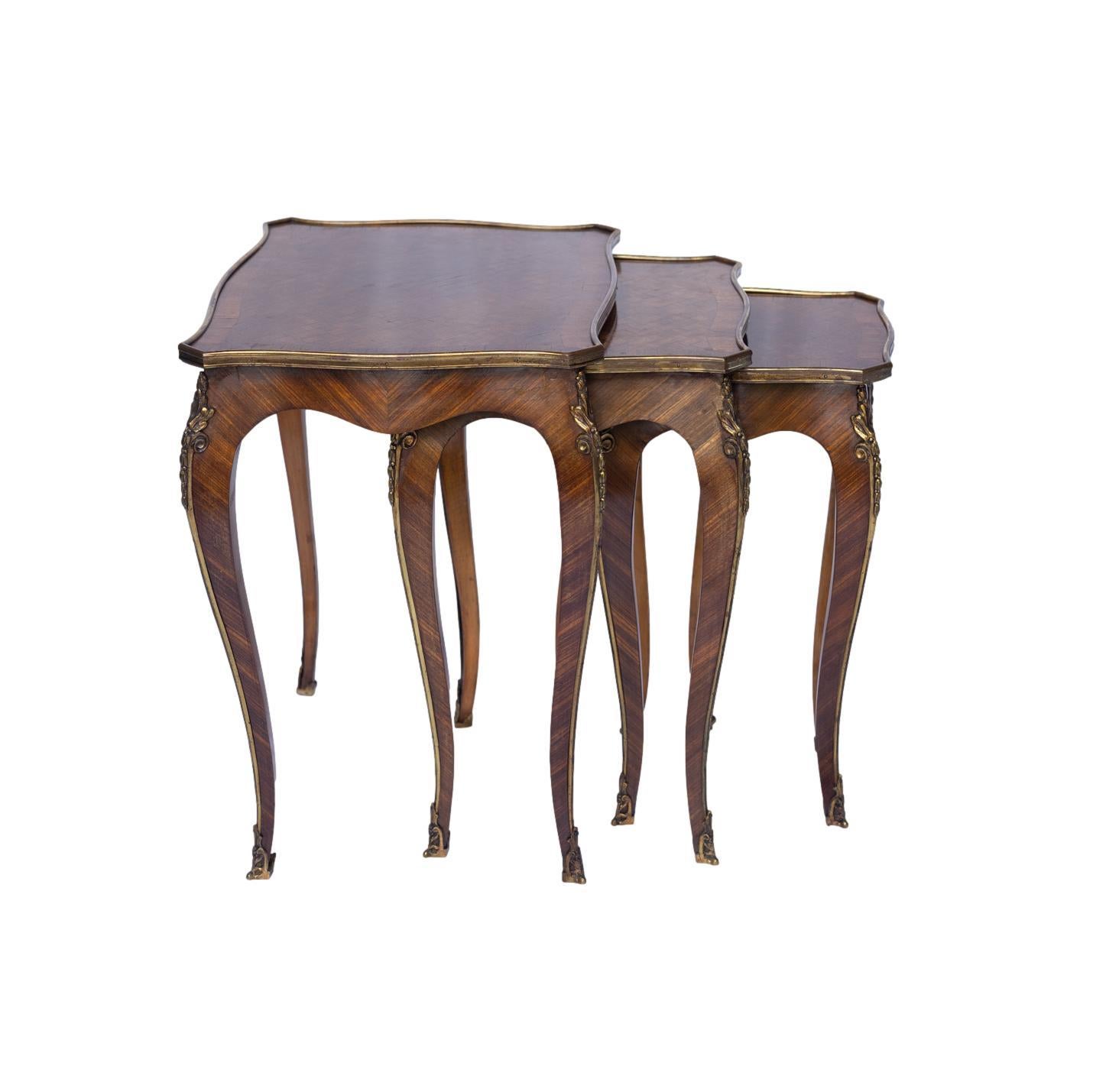 Suite de trois tables gigognes de style Louis XV en bois de roi et parqueterie, chacune avec un plateau rectangulaire façonné et bagué, centré par un panneau de parqueterie et dans un bandeau d'ormolu, reposant sur des pieds cabriole surmontés de