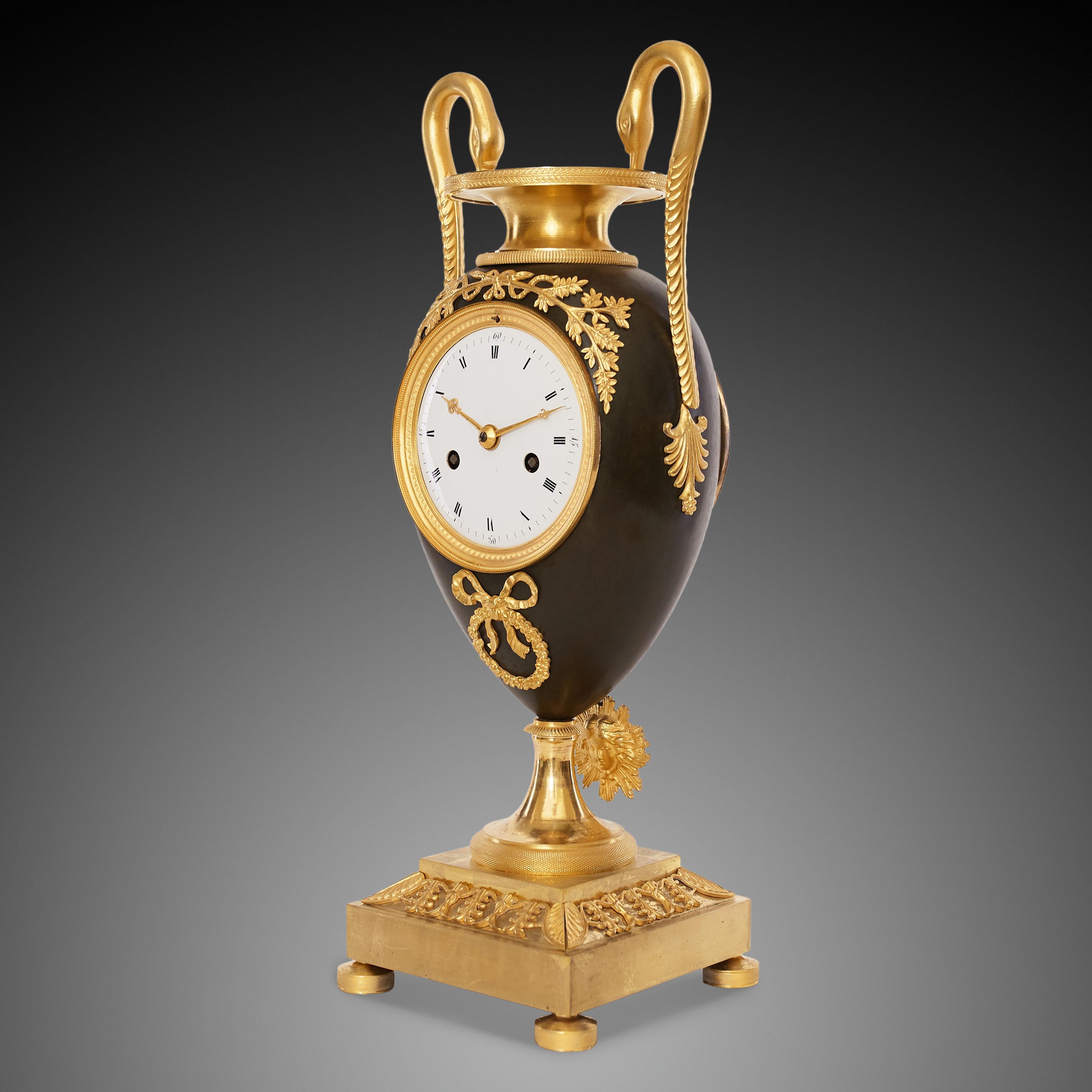 This Etruscan vase-shaped mantel clock cast from bronze with gilded elements and brown patina originated from the first half of the nineteenth century. The Empire style was based on elements of the Roman Empire and its culture, which had been