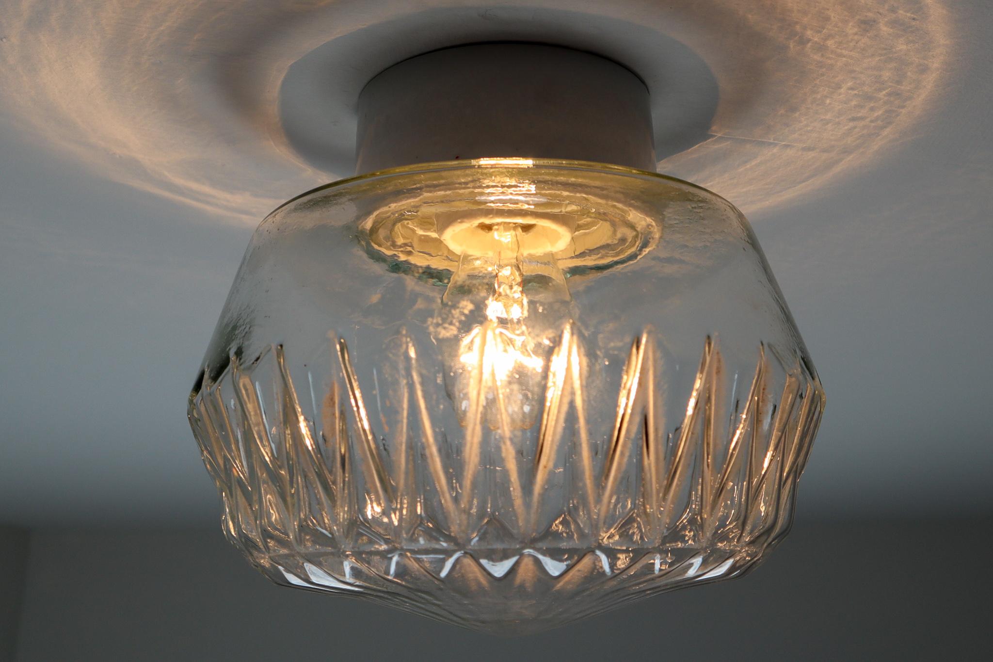 Set of two vintage modern wall /ceiling lights with clear structured glass and porcelain base, France, 1960s. The glass has pattern in it, what gives a nice diffuse light effect and a nice pattern on ceiling and walls, these wall scones/ceiling