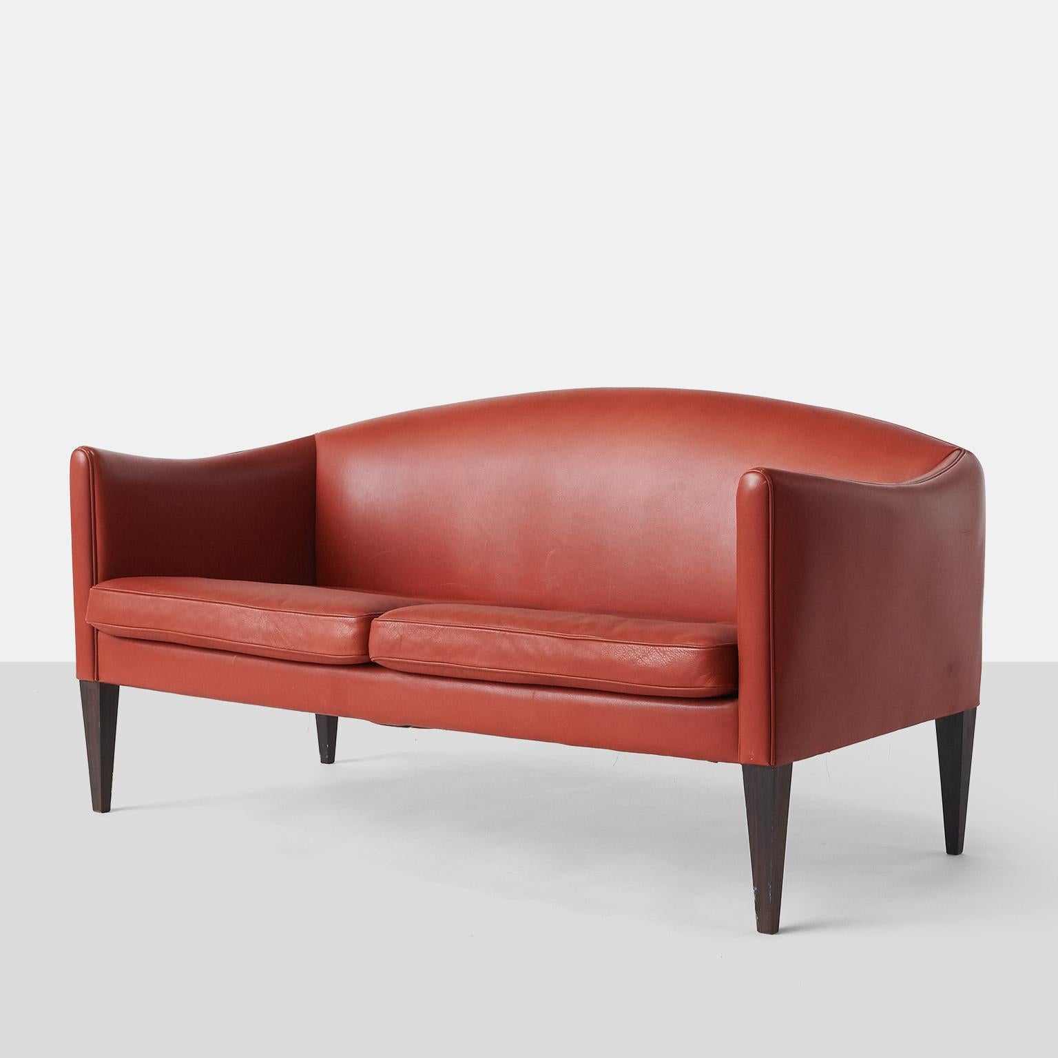 A two-seater sofa with tapered rosewood legs and 2 seat cushions. Upholstered with red leather. Model V12.

Exceptional condition for a piece of this vintage. Very little wear with only very slight abrasions to the arms and near perfection on the