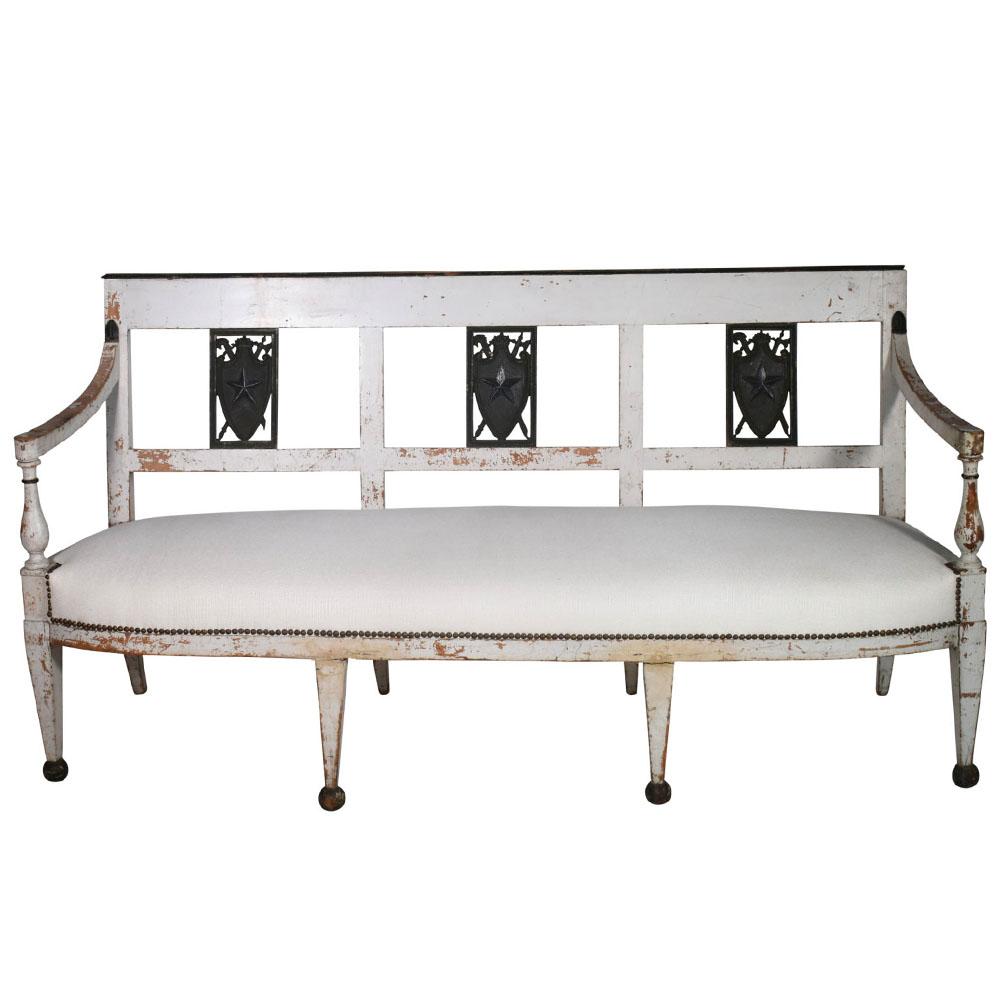 This gorgeous 19th century French Directoire settee has detailed neoclassical coat-of-arms carving with chic proportions and a clean classic style. This French Directoire settee features antique white painted wood. Eight legged, front four with