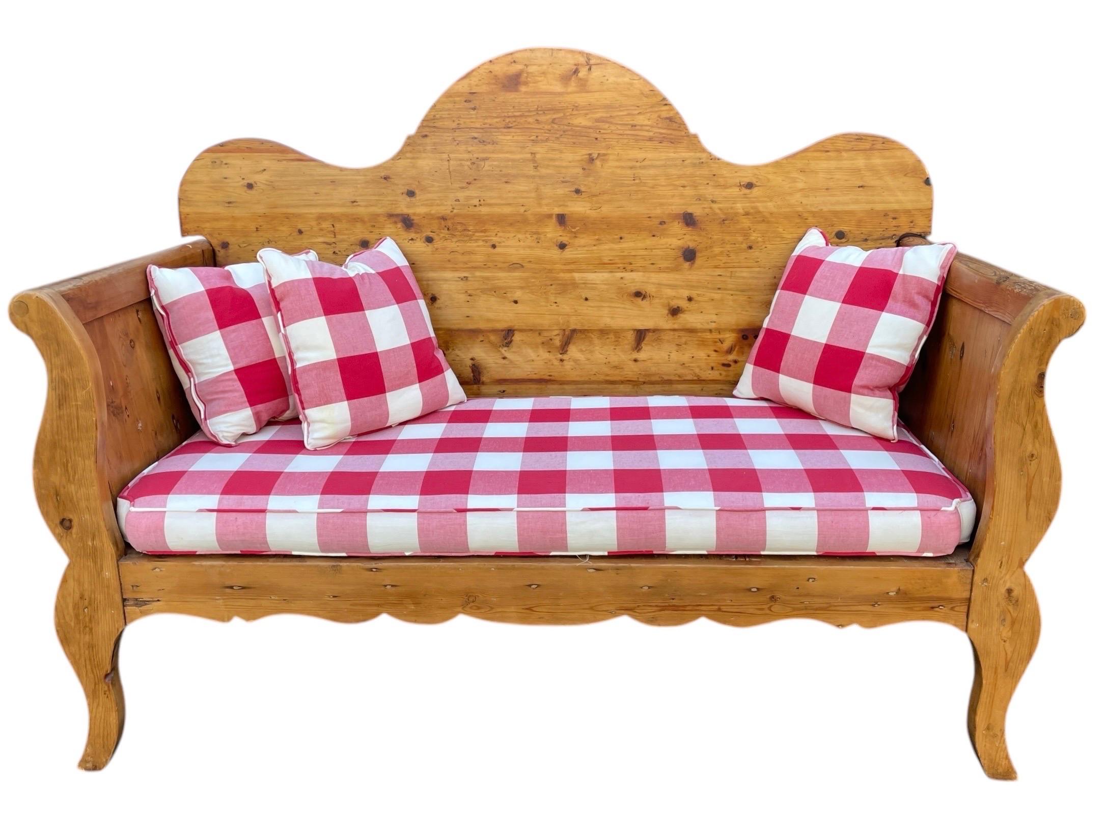 Ce banc est un must avec son dossier à lattes en bois noueux de forme festonnée avec deux accoudoirs à volutes et complété par un revêtement et des coussins à carreaux rouges et blancs. L'ensemble repose sur des pieds courbes. Une pièce unique et