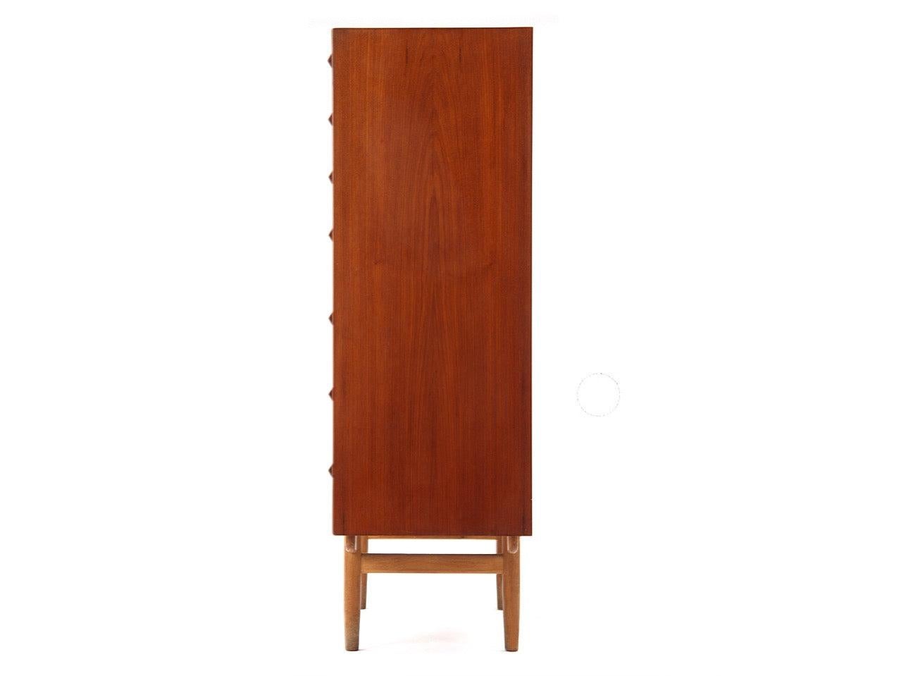 Comò alto a sette (7) cassetti in teak con maniglie in legno integrate su una base in Oak con gambe a tasselli affusolati.