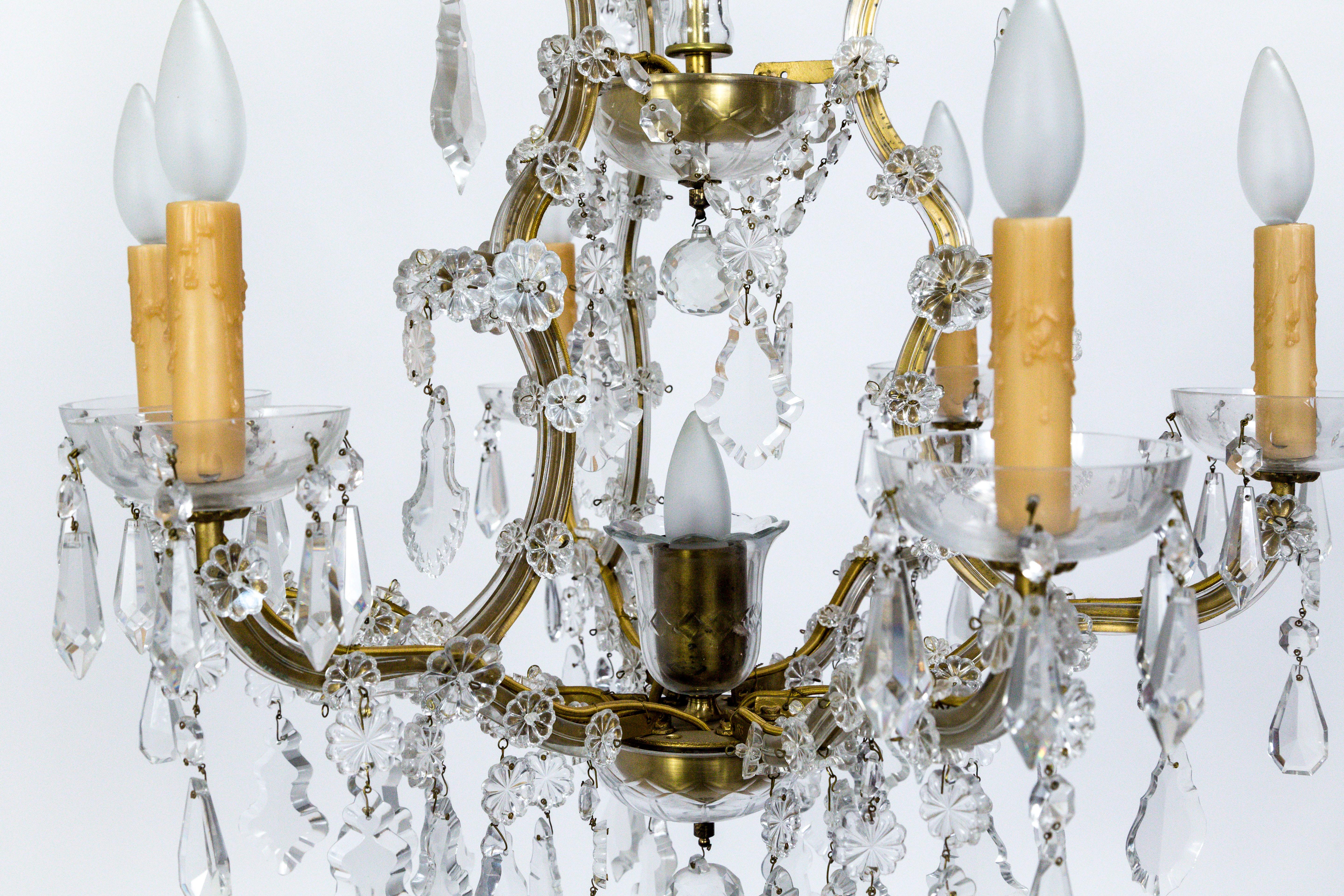 Created in the 1920s, this chandelier is beautiful example of the late 18th century Austrian Empress Maria Theresa style; with crystal strips on the raw brass arms. Decked with Pendalogue, drop, and flower crystals, and molded glass bobeches and