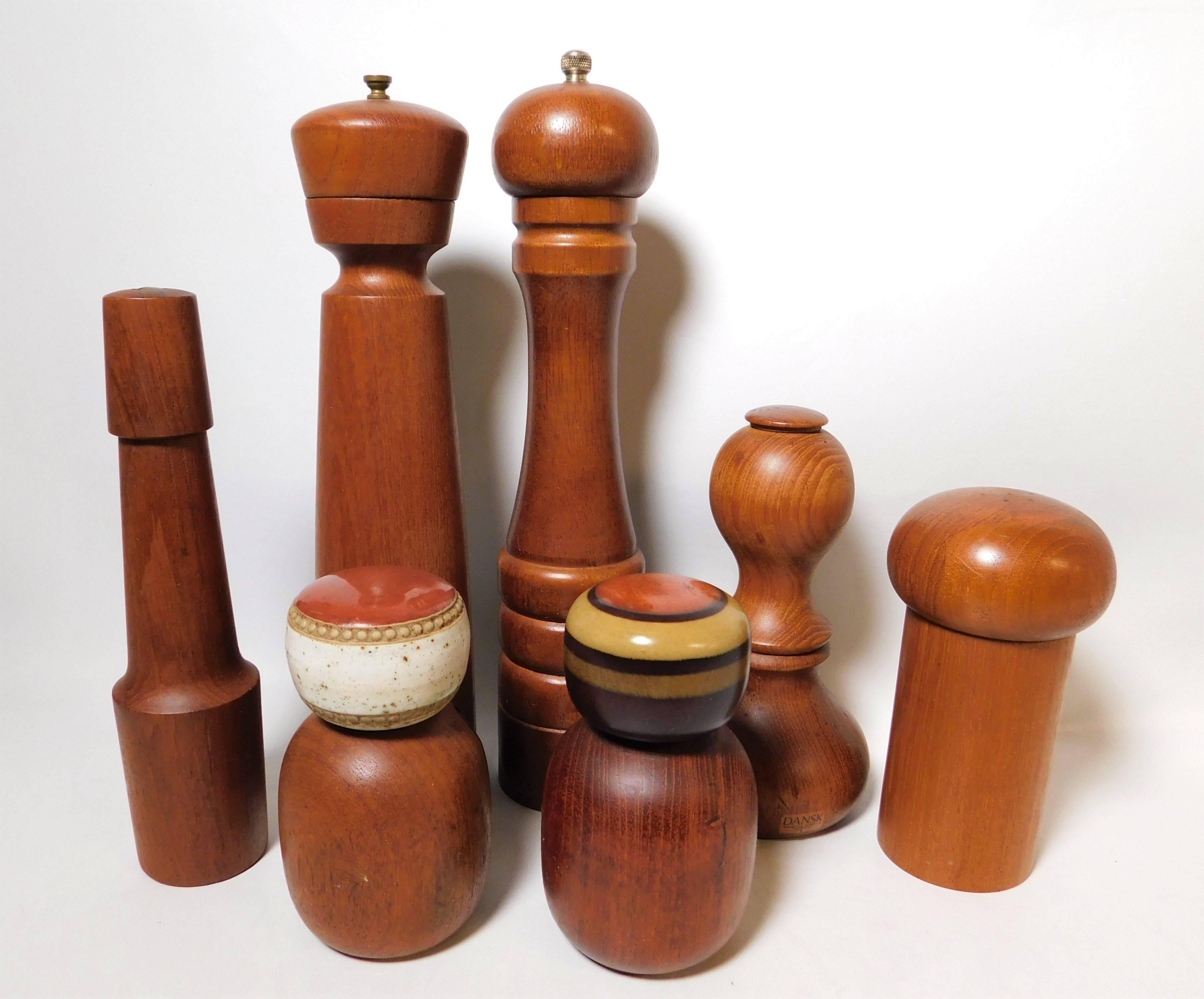 These seven teak pepper mills and salt grinders consist of three pairs and one single. The Italian pair have porcelain tops and measure 5.25 inches x 3 inches round. The tallest pair measure 11 inches x 3 inches round. The wood pair measures 7