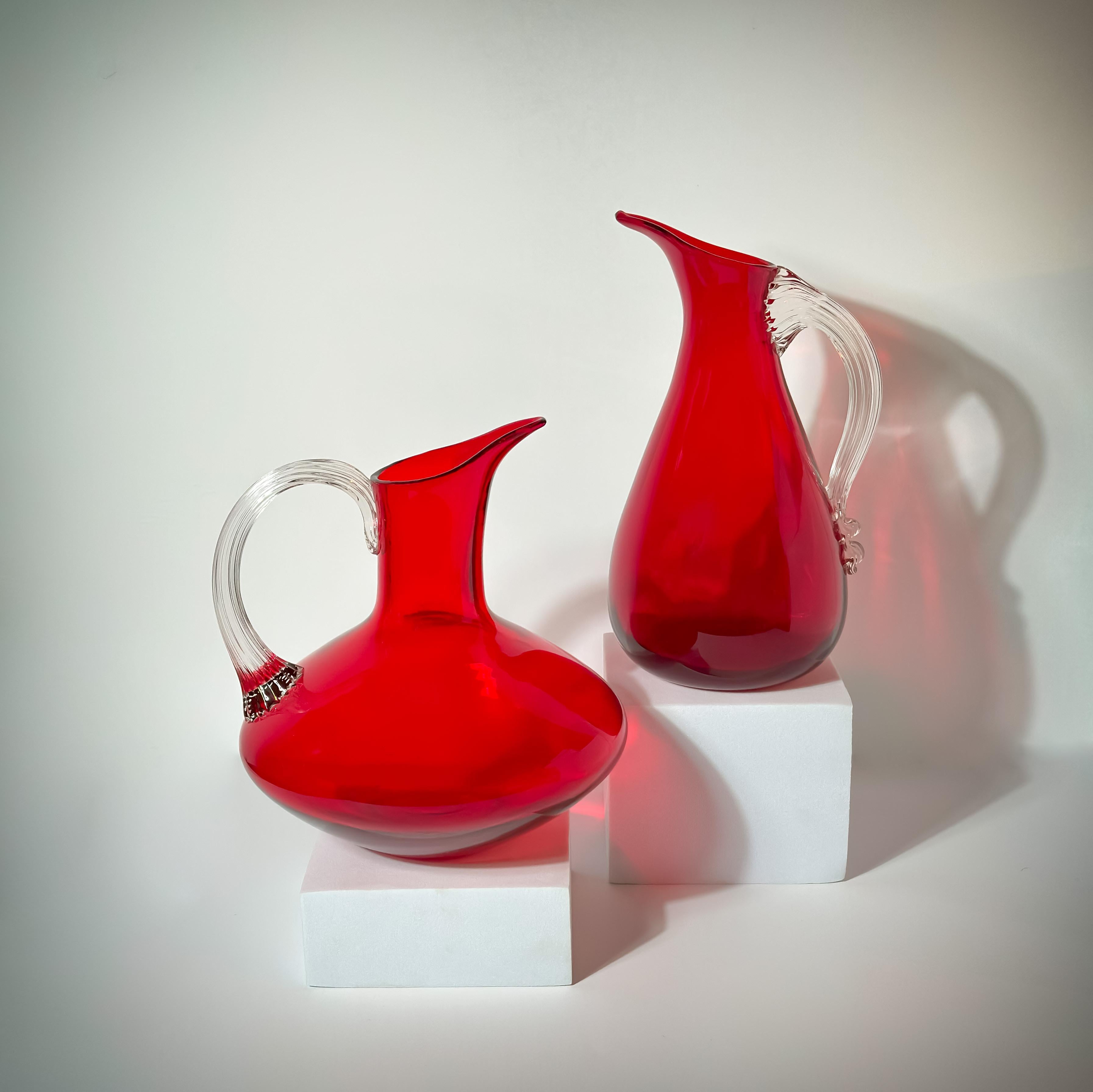A set of seven ruby red glass jugs, crafted by renowned English glassmakers Whitefriars and designed by Geoffrey Baxter. 

Released in the 1950s, these “sparrow beak” glass jugs quickly became iconic pieces of decorative glassware in Britain,