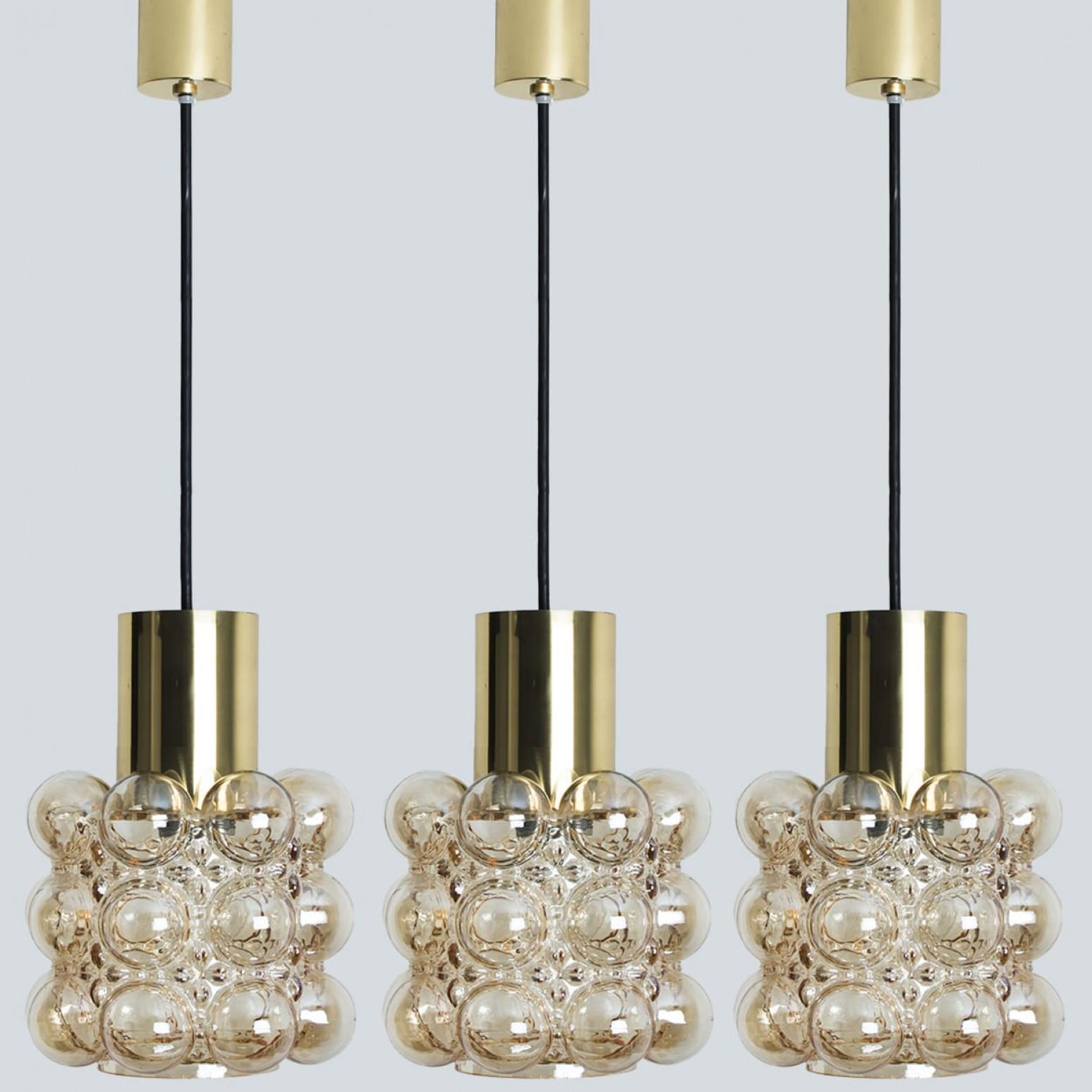 Tre bellissimi lampadari o lampade a sospensione in vetro a bolle d'aria disegnati da Helena Tynell per Glashütte Limburg. Un classico del design, il vetro soffiato a mano di colore ambrato/tonico dona una meravigliosa luce calda.

Il prezzo si