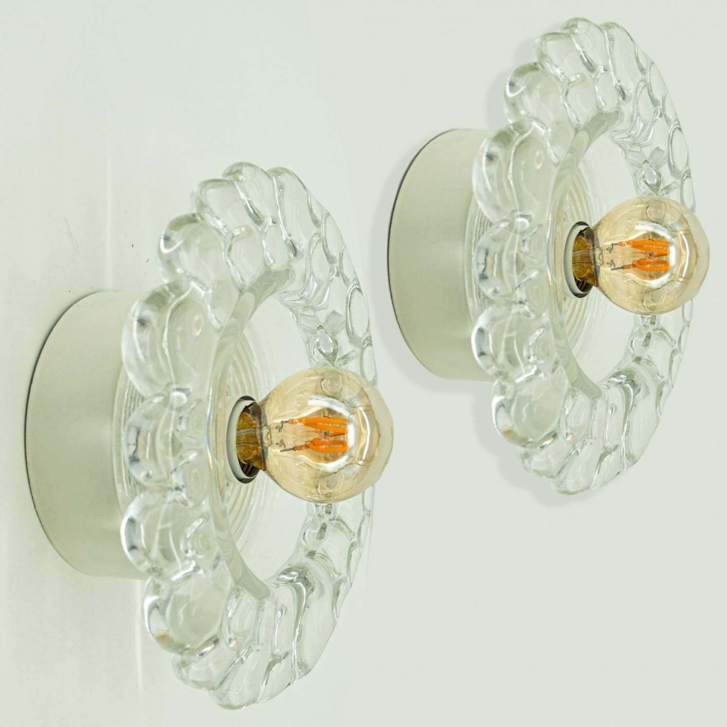 
Varios apliques Putzler de cristal de burbujas sobre armazón redondo de metal, hacia la década de 1970, Alemania. Un diseño claro, con materiales modernos.

Este diseño modernista se centra en el grueso cristal redondo texturizado; cuando se