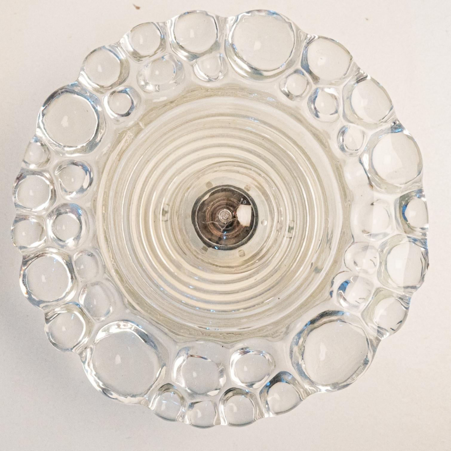 
Varios apliques Putzler de cristal de burbujas sobre armazón redondo de metal, hacia la década de 1970, Alemania. Un diseño claro, con materiales modernos.

Este diseño modernista se centra en el grueso cristal redondo texturizado; cuando se