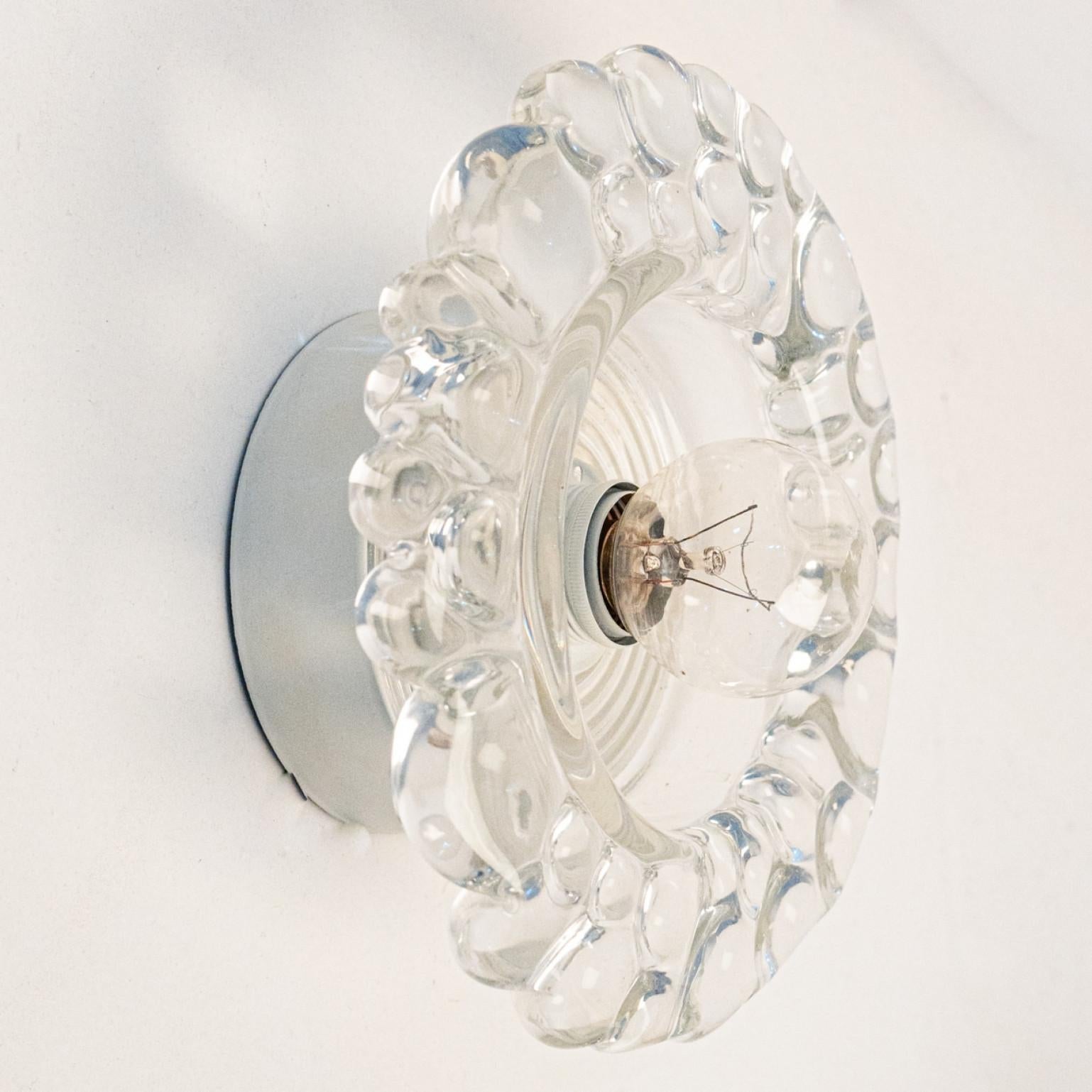 
Plusieurs appliques Putzler en verre bullé sur une monture ronde en métal, vers les années 1970, Allemagne. Un design clair, avec des matériaux modernes.

Ce design moderniste se concentre sur le verre épais rond et texturé. Lorsqu'il est éclairé