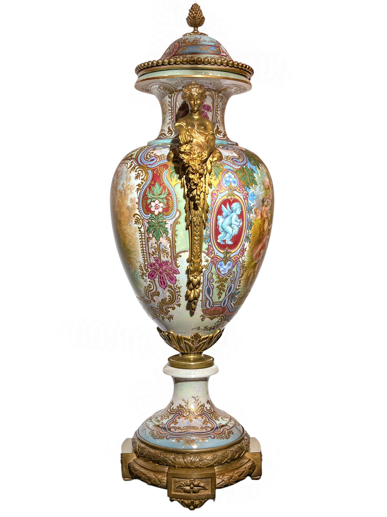 Espectacular urna de Sèvres, muy ornamentada, de estilo Art Nouveau. Escenas de jardín hábilmente pintadas a mano de doncellas y putti a ambos lados con flores de vivos colores, follaje, formas de volutas y algunos pequeños retratos que las