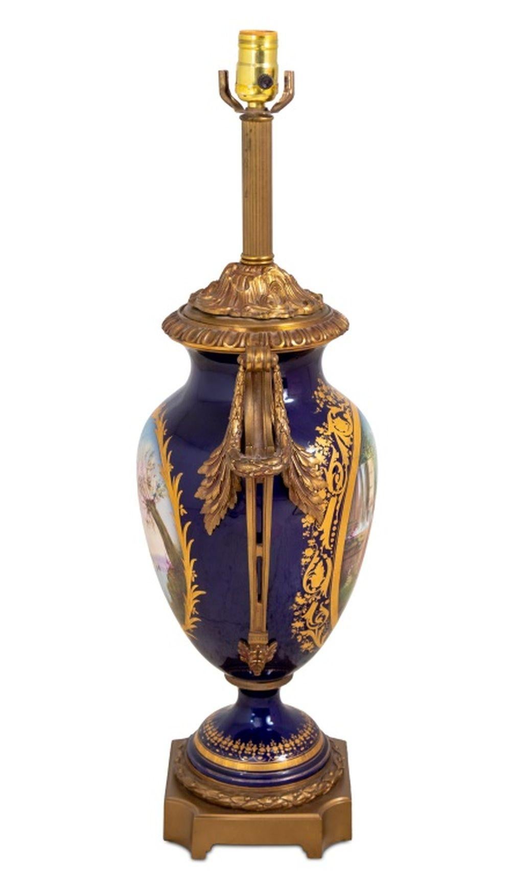 Blaugeschliffene Porzellanvase aus Sèvres als Lampe, frühes 20. Jh., mit vergoldeten Metallgriffen, der eiförmige Korpus bemalt mit einer Szene von Reisenden in einer Landschaft und einer bukolischen Seeszene, signiert 