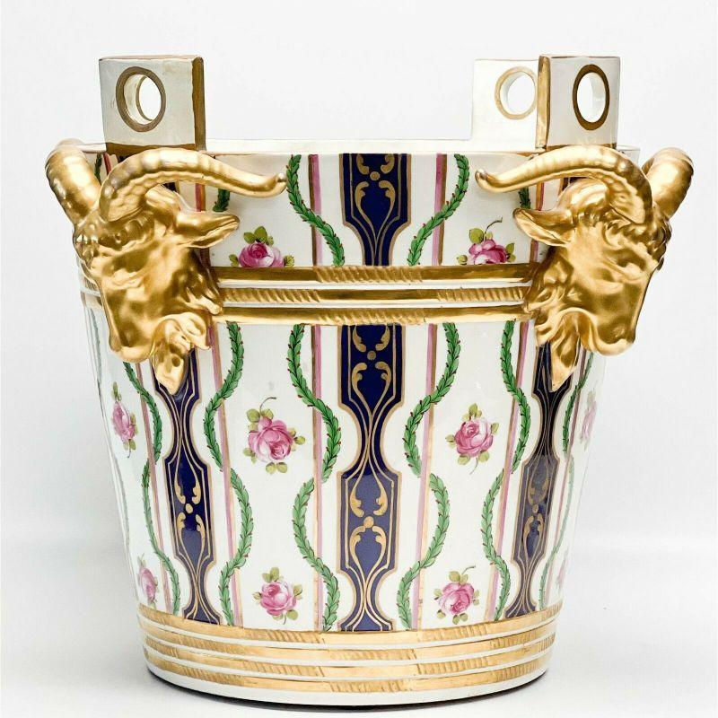 Sevres France hand painted porcelain rams head jardiniere or cache Pot, late 19th century.

A white ground with colorful florals and leaf decoration with gilt bands, cobalt blue stripes with gilt foliate designs. Four gilt figural rams heads