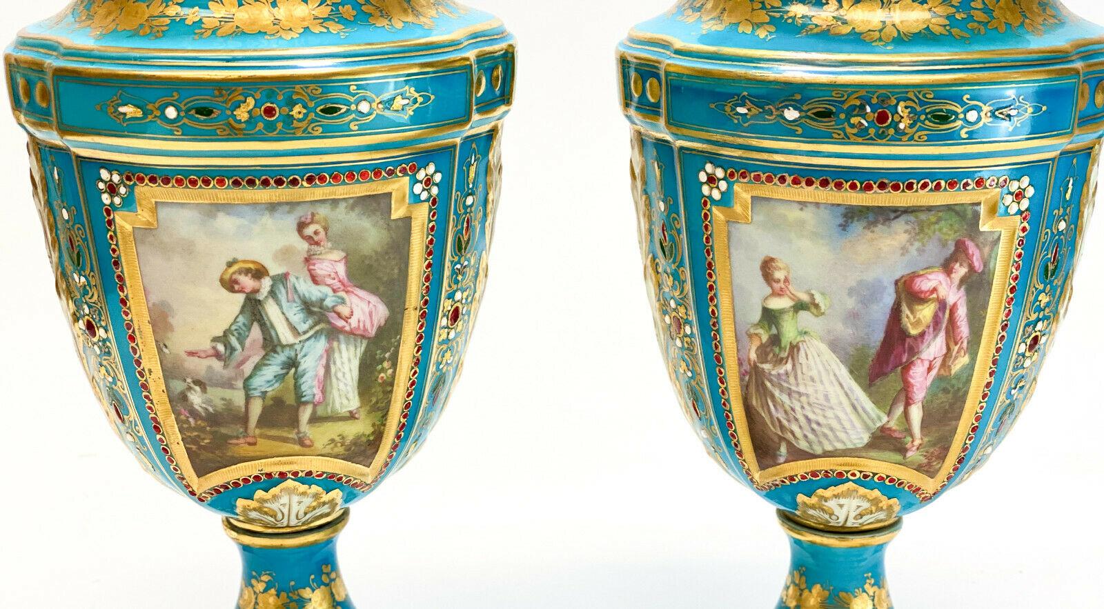 A pair of Sèvres porcelain hand painted jeweled enamel lidded urns, 19th century. A turquoise blue ground with hand painted courting scenes to the central area and floral bouquets to the verso. Applied red jeweled accents throughout. Marked for
