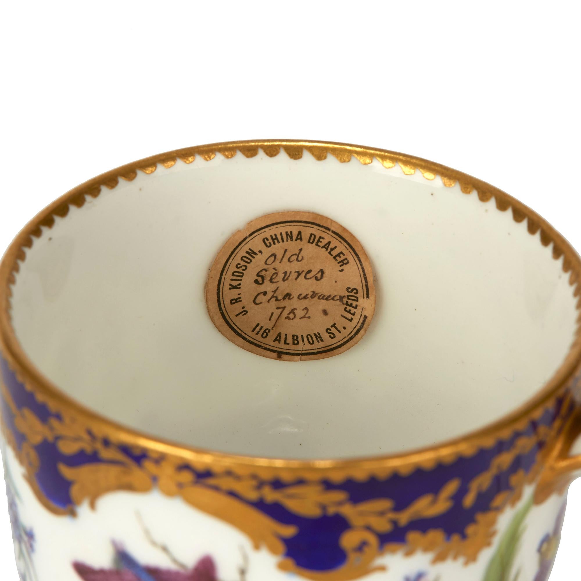 A rare and exceptional antique Sèvres soft paste porcelain cabinet teacup hand painted with birds landscapes interspersed with floral designs on a white ground within cobalt blue borders finely gilded with scroll and leaf designs dating from circa
