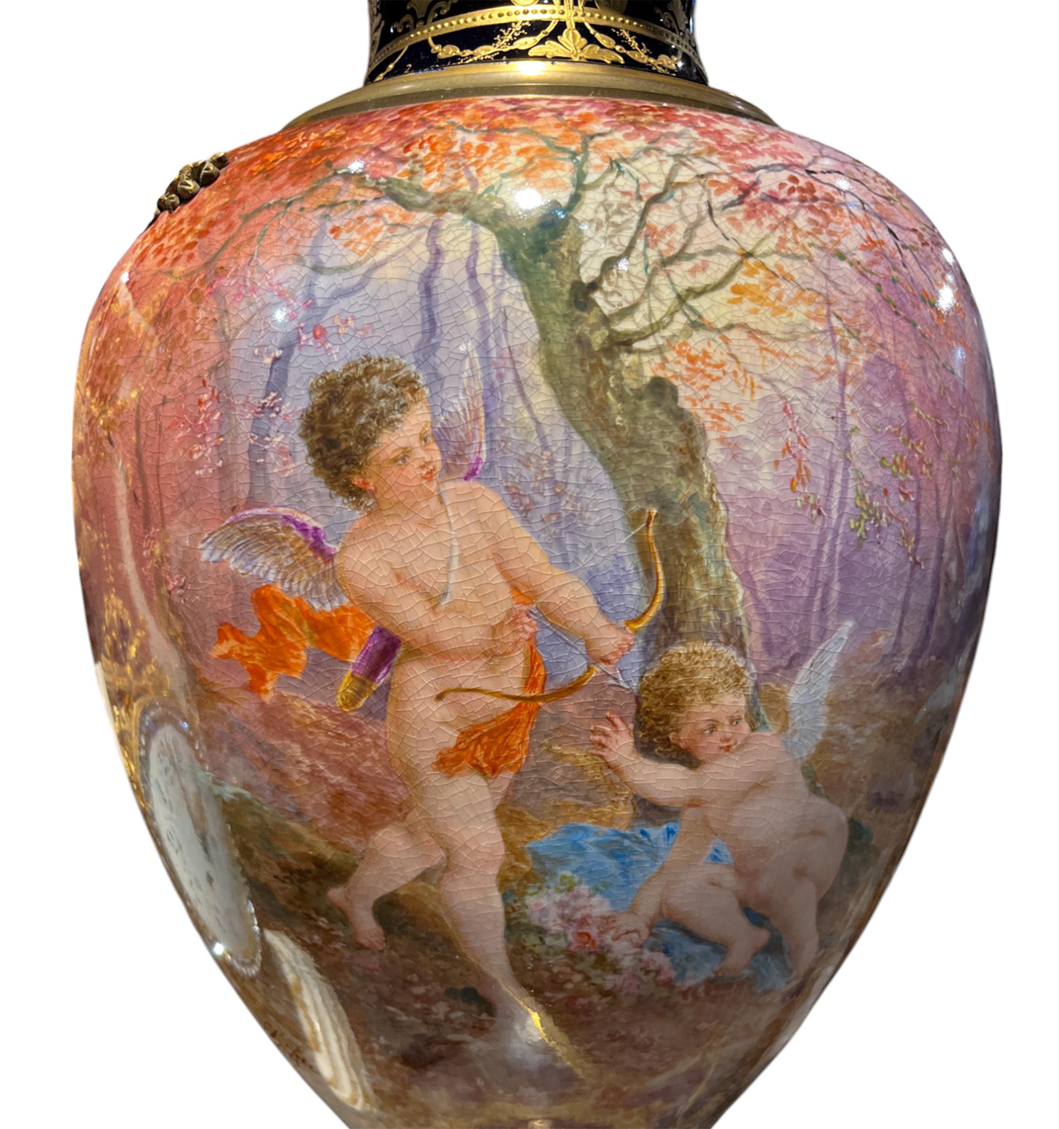Sevres Ormolu-Mounted Covered Vase of impressive size depicting cupid and two cherubs in a lush and colorful garden on both sides. The glazed painting applied bursts with bright and bold pinks, reds, yellows and blues on the front that diffuse into