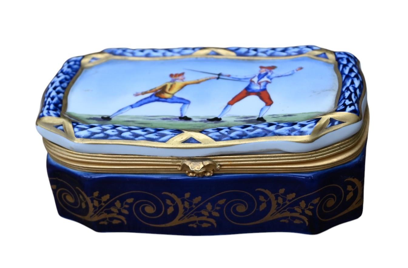Boîte en porcelaine bleu cobalt et feuille d'or avec des montures en métal doré et un décor d'escrimeurs sur le couvercle.
Peint à la main et marqué à l'intérieur du couvercle.
7,2 x 12,7 cm, hauteur 4,7 cm.