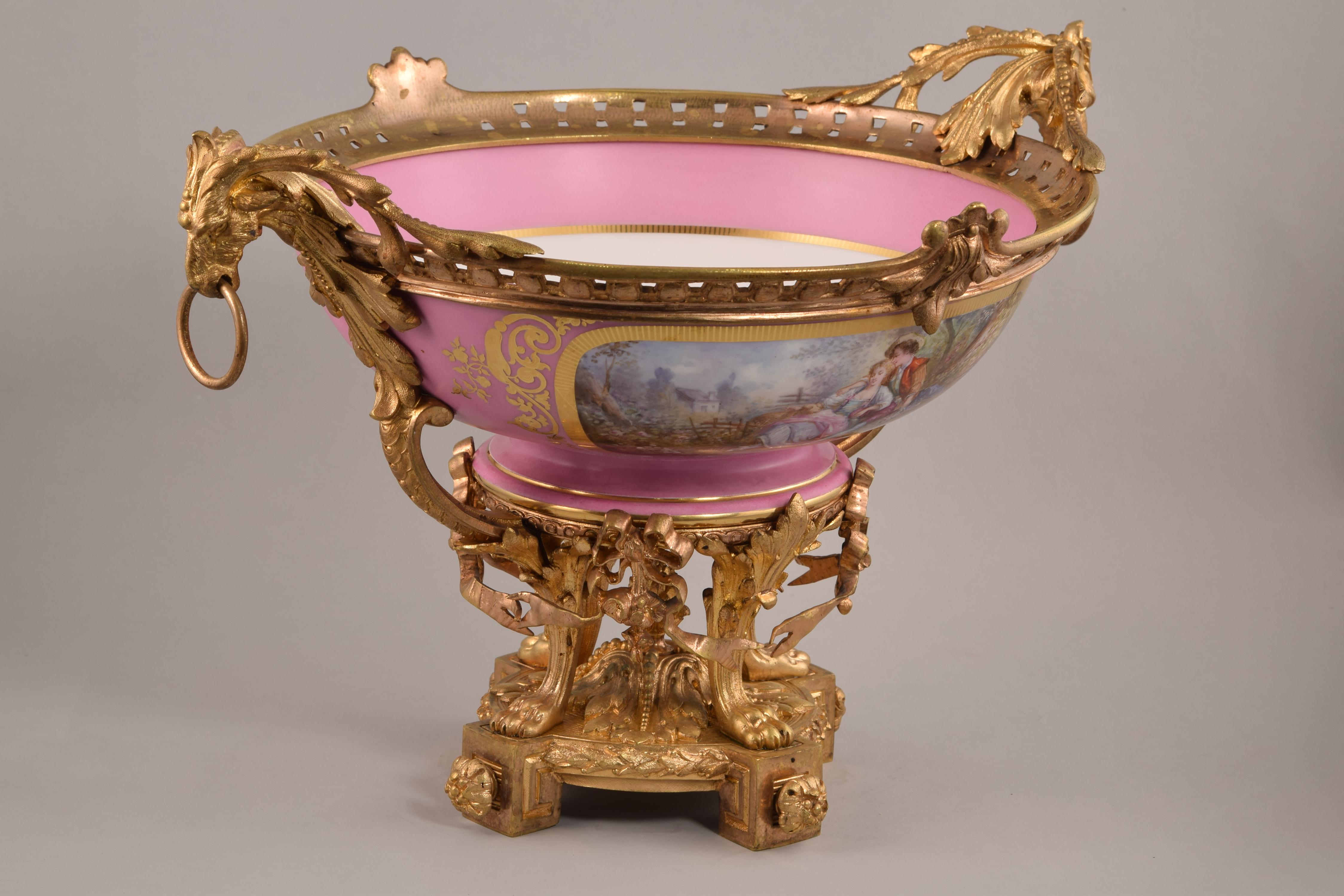 Sèvres porcelain centerpiece. Enameled porcelain and gilt bronze. France, 1885. 
 With markings on the base (porcelain). 
 Centerpiece with porcelain piece enameled in a pink tone, with gilding and figurative scenes, and gilt bronze frame
