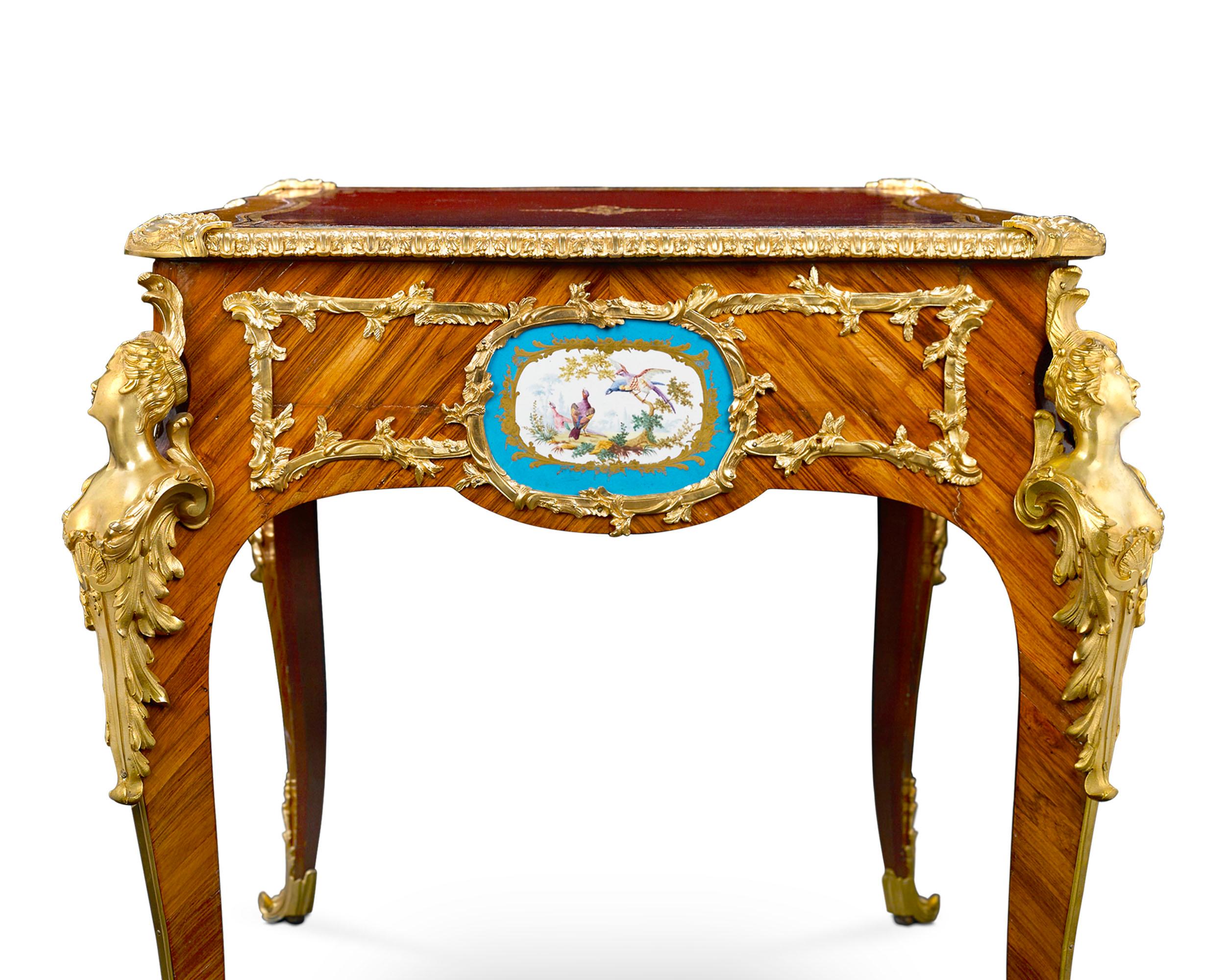 Form and function converge in this exceptional Louis XV-style bureau plat graced with eight elegant Sèvres Porcelain plaques. Framing these delightful, hand painted floral and fowl-themed plaques is a network of exquisite gilt bronze. Supporting the