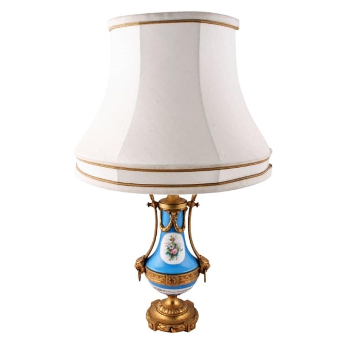 An late 19th century Sévres porcelain and ormolu table lamp.

The urn shaped Sévres porcelain has a blue background with decorative panels of birds and flowers.

The vase is held in an ormolu frame consisting of a circular wreath shield base