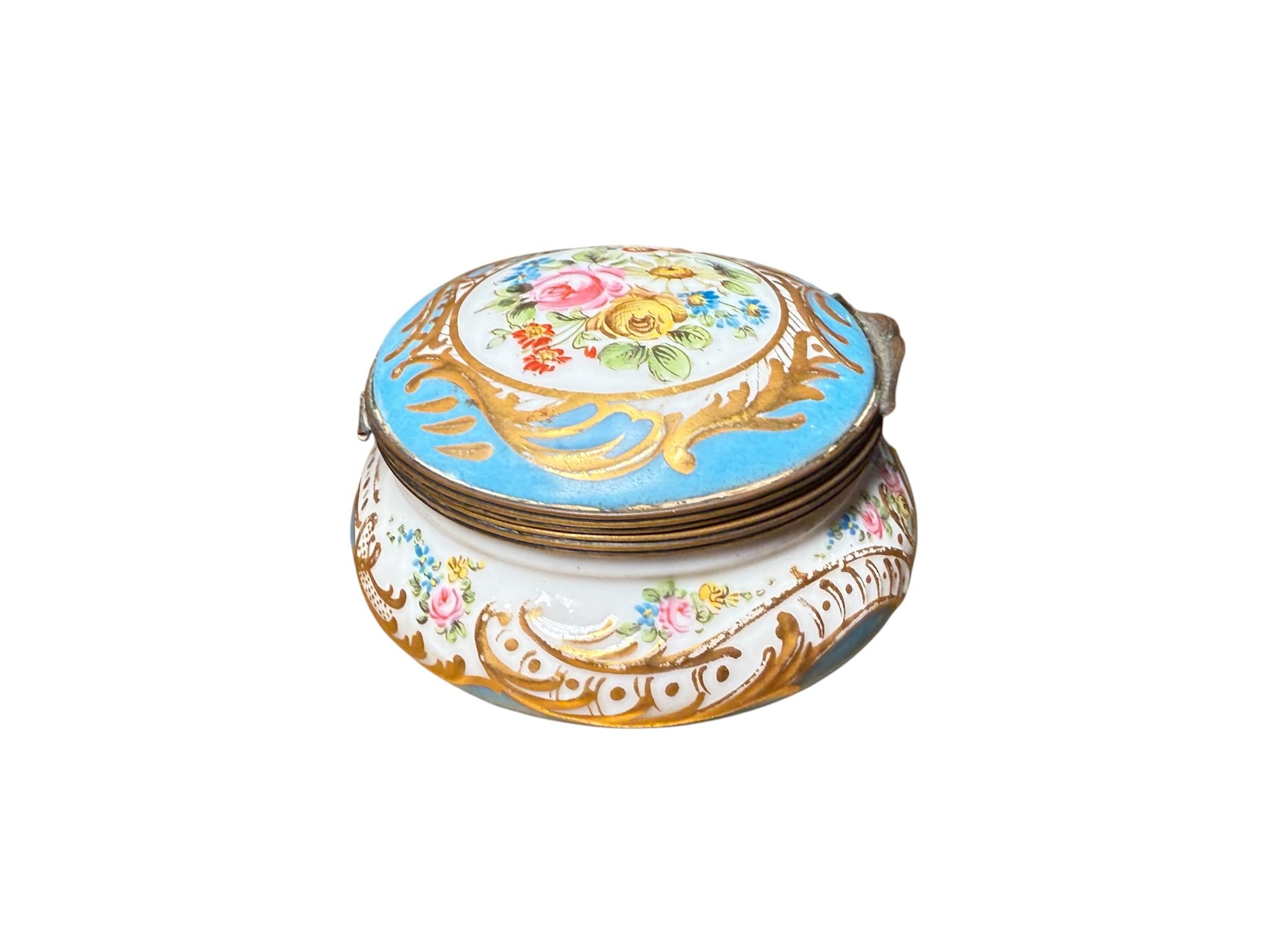 This is a Sevres Porcelain Trinket Box. It depicts a round trinket box hand painted turquoise and white color adorned with a bouquet of flowers at the center of its hinged lid. Hand painted gold color scrolls framed the bouquet. Branches of pink and