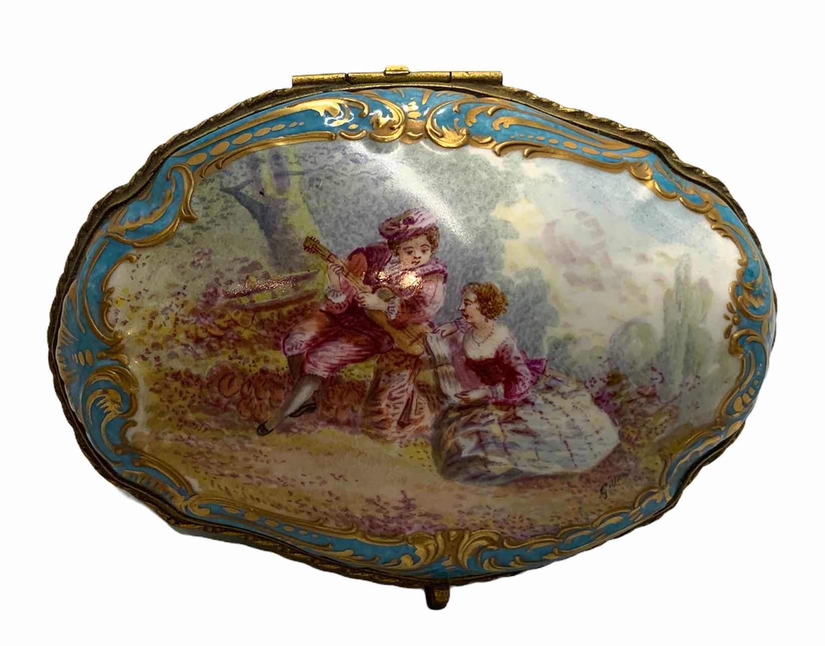 This a porcelain trinket box hinged lid depicting a hand painted 18th century pastoral scene of a young boy learning to play a guitar while his teacher is teaching him the musical notes. The scene is framed with gilt scrolls over a turquoise