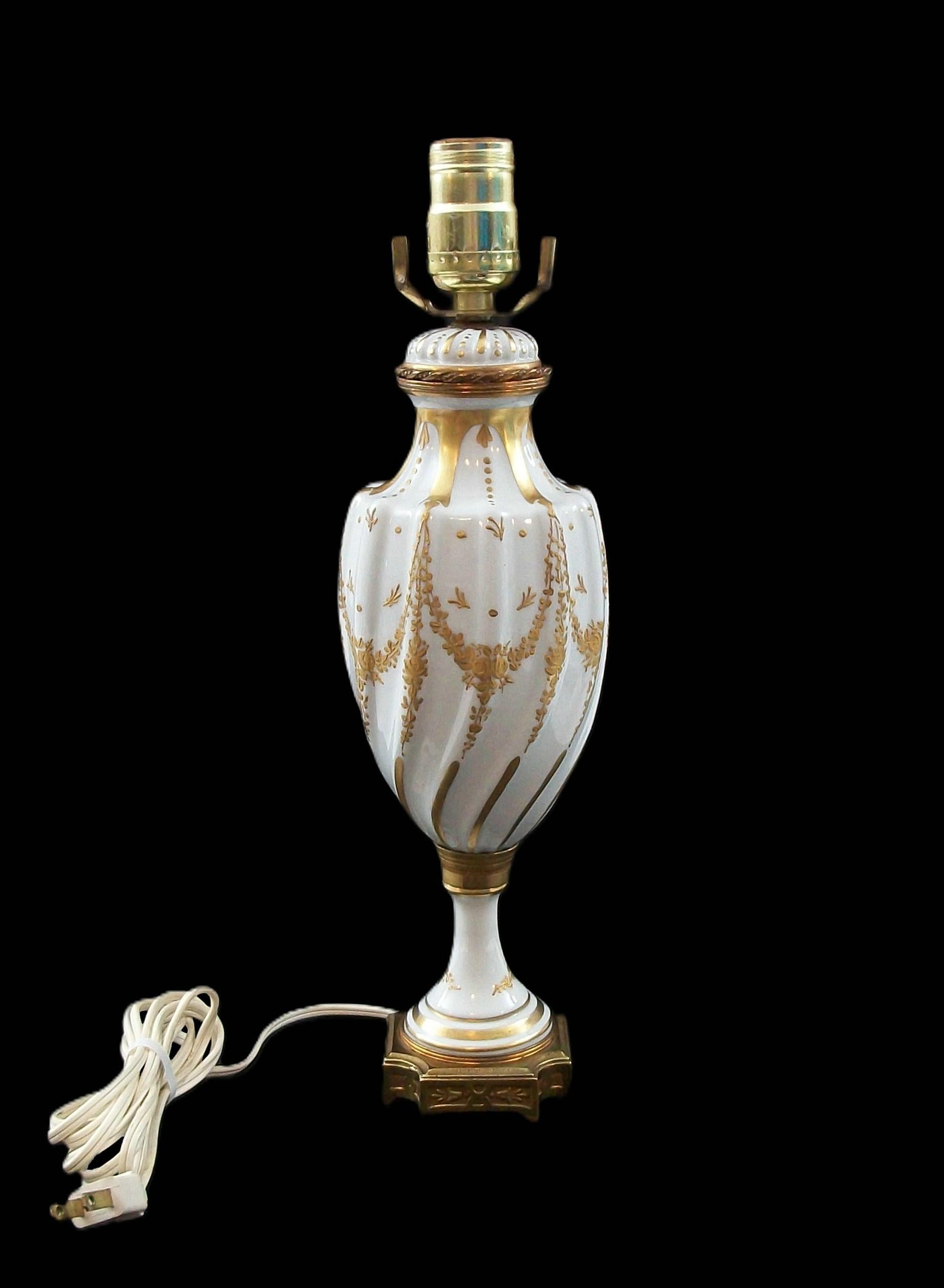 Lámpara de estilo Sevres pintada a mano y dorada - presenta una forma retorcida y acanalada con decoración floral en relieve - todo ello sobre fondo esmaltado blanco - base y soportes de latón - firmada en la base (pseudo marca Sevres), Pintada a