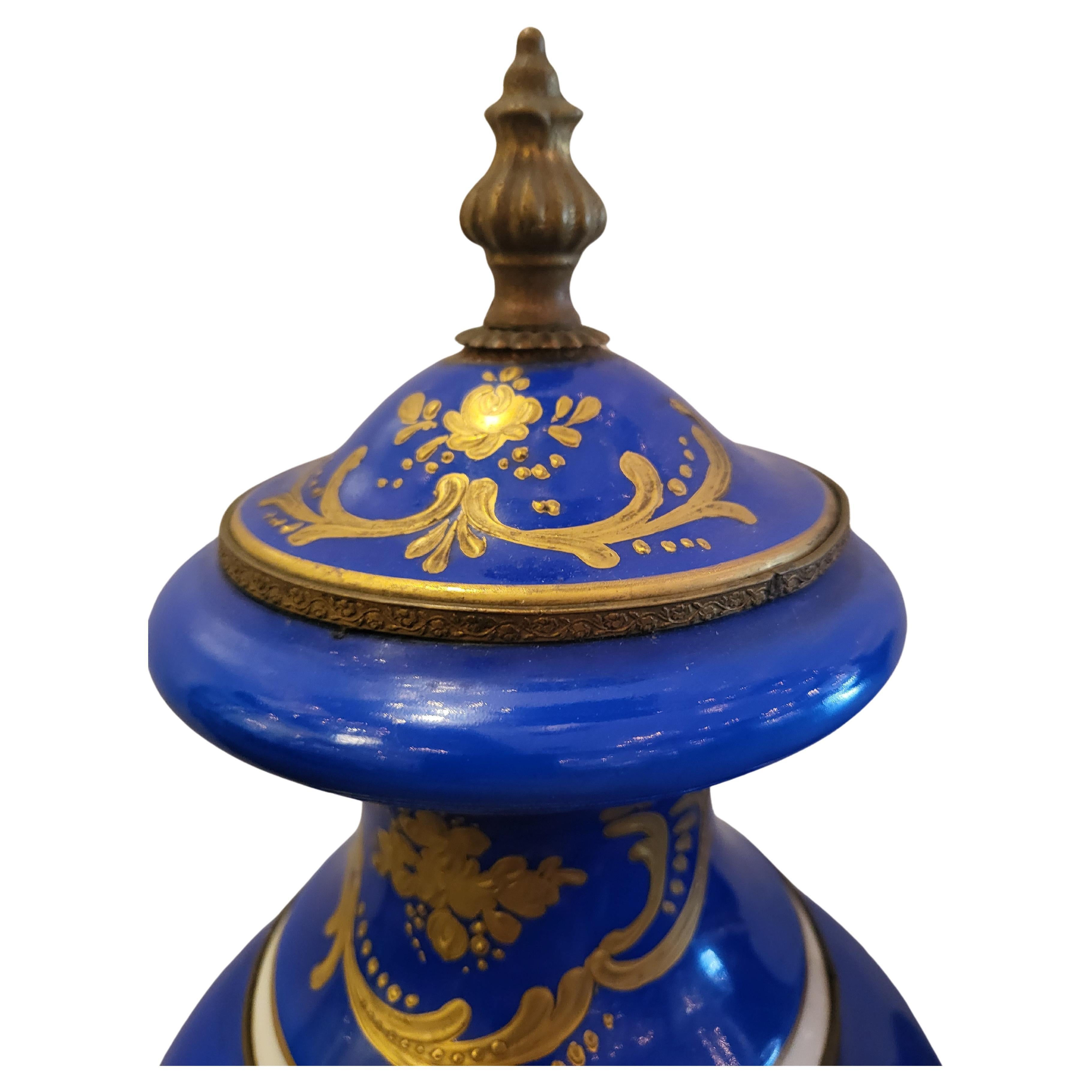 Sevres style porcelain bolted urns, 19th c., royal blue ground, raised gilt enamel, hand-painted reserves with flowers, fluted plinth, rising on gilt metal feet.