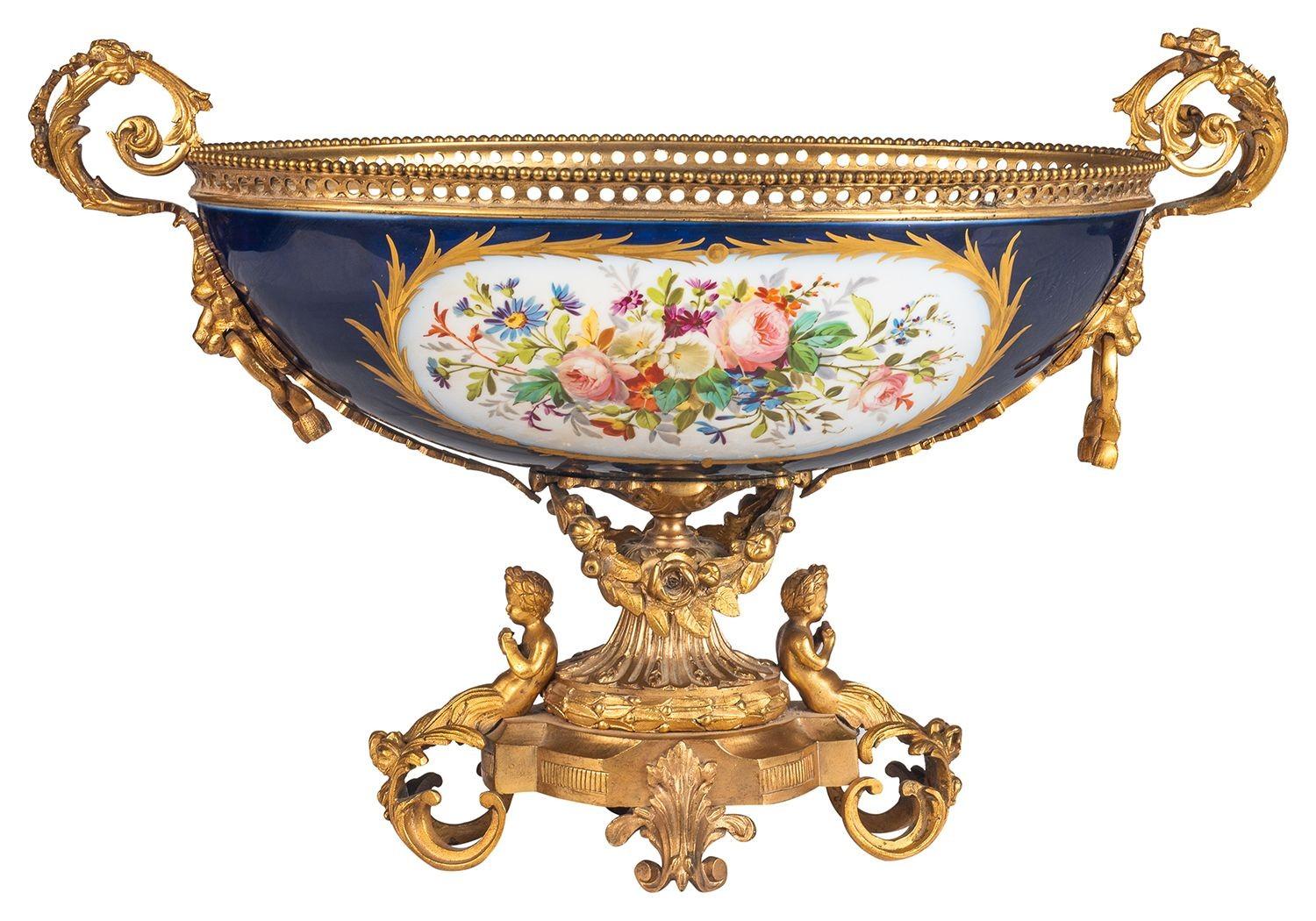 A very good quality French Sevres porcelain comport, having wonderful gilded ormolu scrolling foliate mounts, with cherubs seated , the cobalt blue ground porcelain with inset hand painted panels depicting a scene of a young lady being taught to