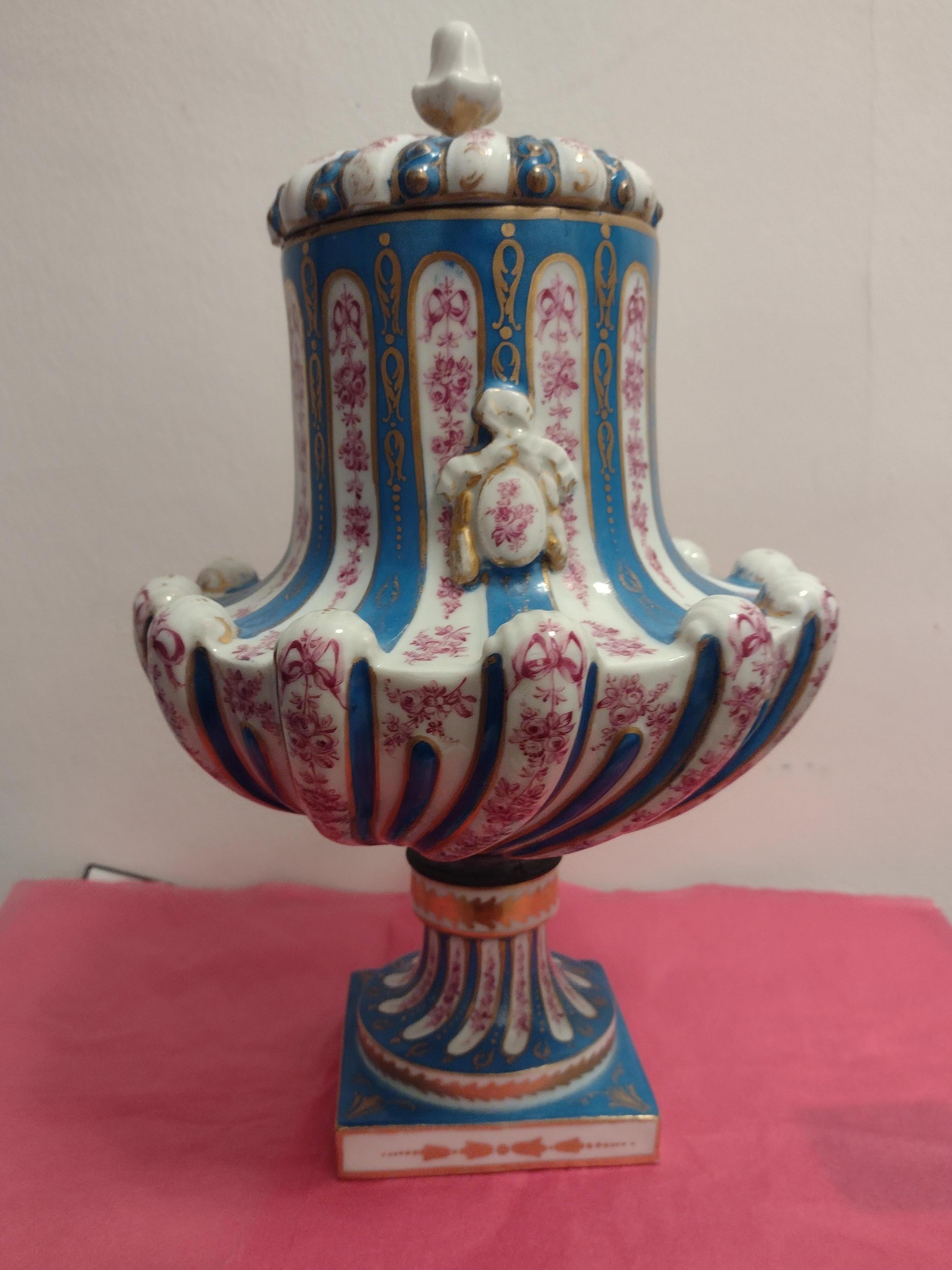A Sevres style porcelain covered vase early 20th century. The wrythen body surmounted by domed lid, decorated with ribbon tied trailing foliate ornament, raised on  on square plinth, pseudo blue painted interlaced