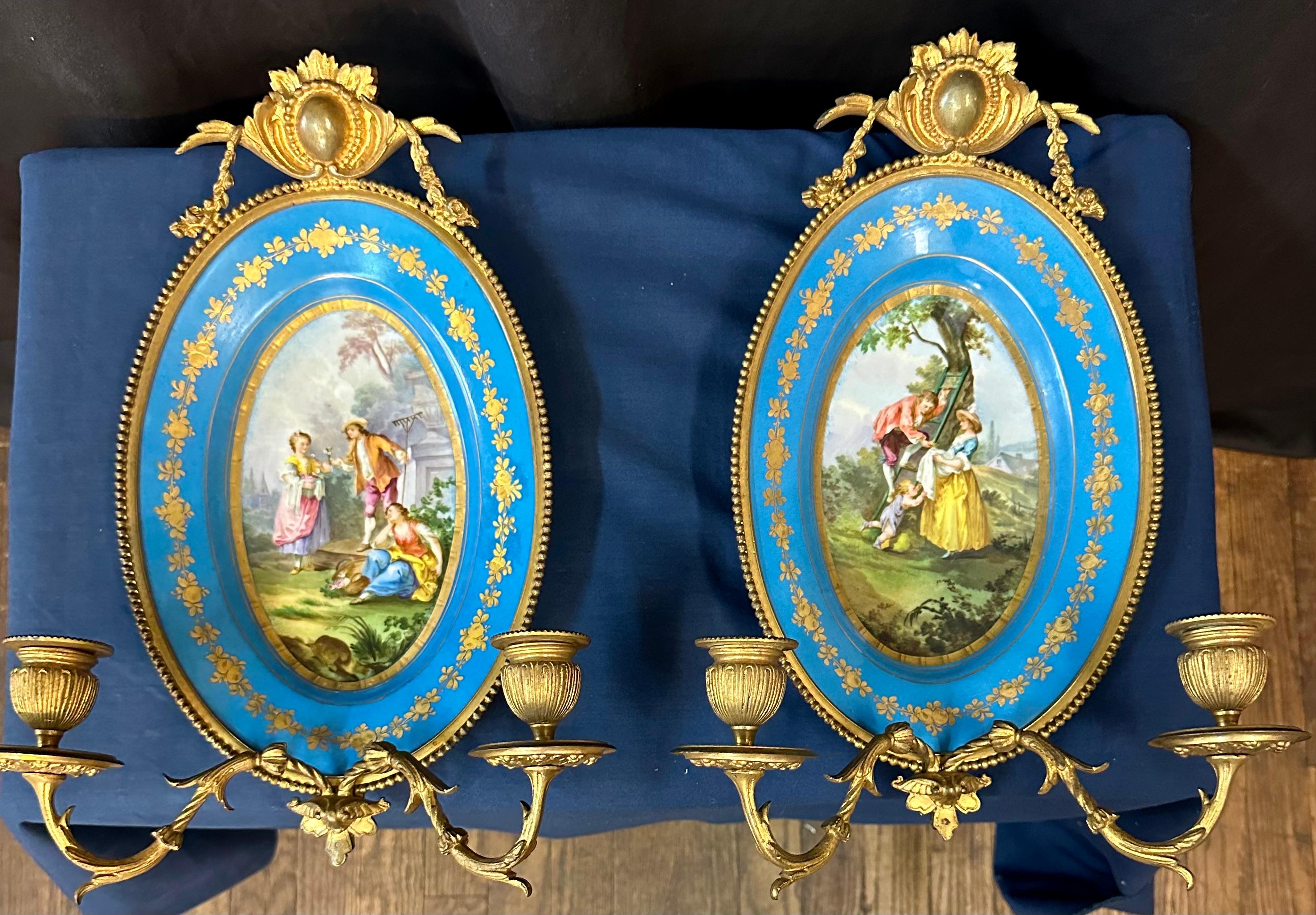 Dieses atemberaubende Paar Wandleuchter aus Sèvres-Porzellan stammt aus dem frühen 19. Jahrhundert und zeigt feine handgemalte Porzellanszenen  mit scharfen, lebendigen Details. Diese lebhaften, ovalen Gemälde werden durch tief himmelblaue Ränder