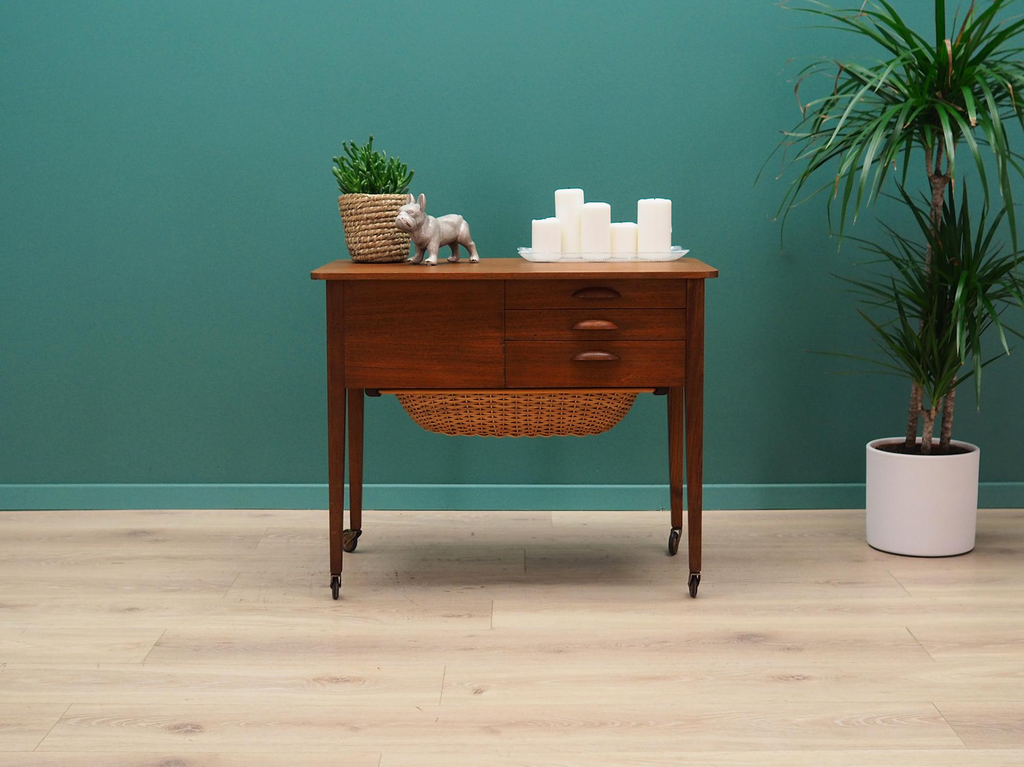 Fantastic sewing table from the 1960s-1970s. Danish design, Minimalist form. Surface covered with teak veneer, legs made of solid teak wood. The furniture has three drawers on the front and one on the side. Additionally, a rattan basket is mounted