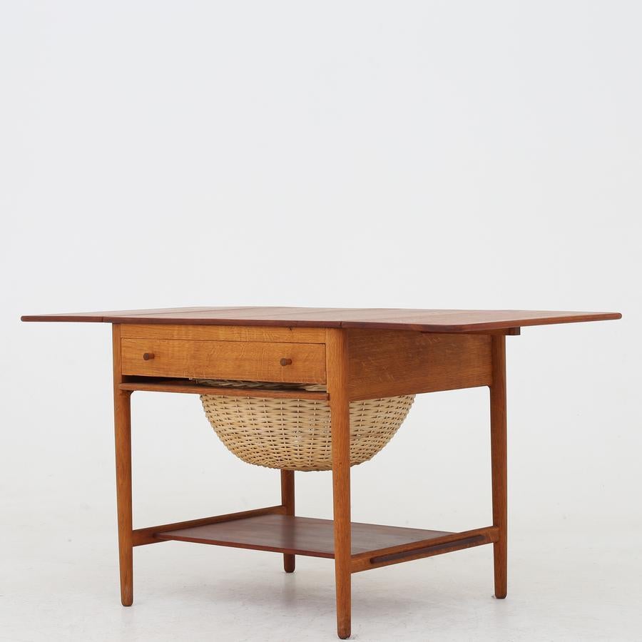 AT 33 - Sewing table with teak top and patinated oak frame. Wicker basket. Maker Andreas Tuck.