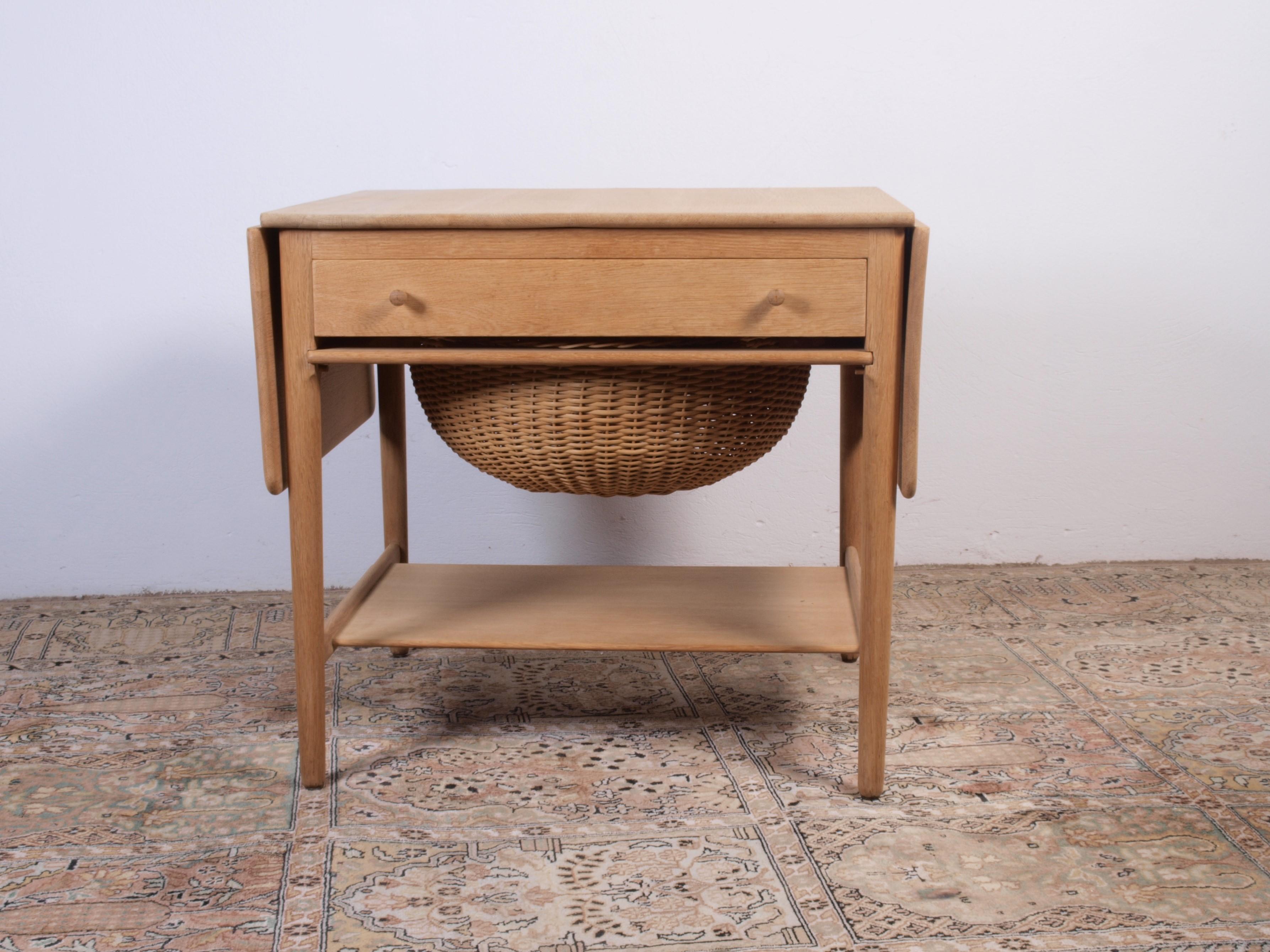 Offering a sewing table crafted from solid oak, this is the iconic Model AT33. The front of the table features a drawer with its original fittings, including holders for bobbins, and a woven wicker basket for yarn. Additionally, there's a lower